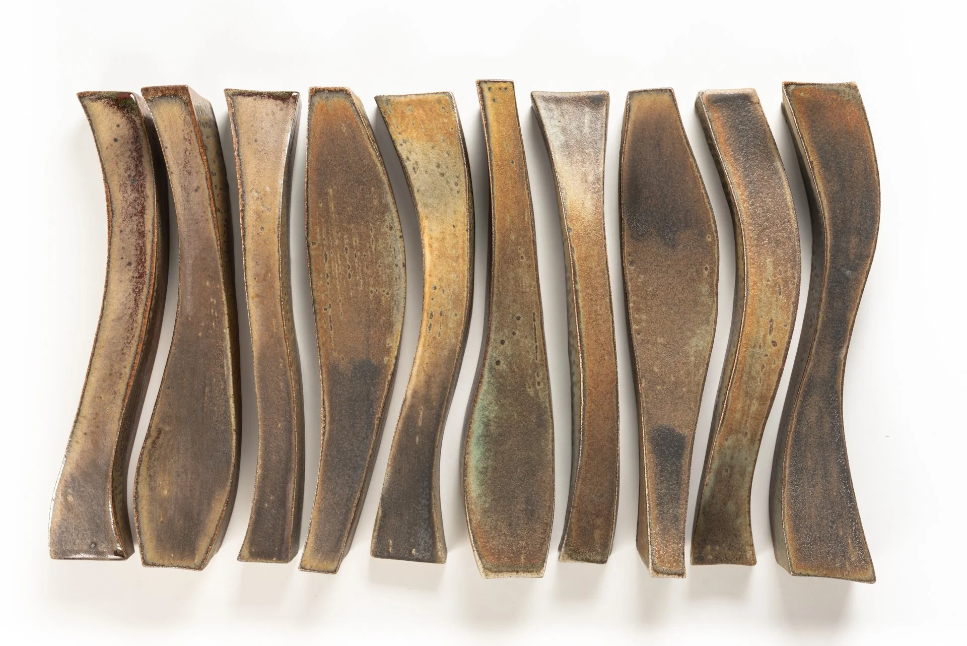 Set of ten organic vertical sculptural pieces arranged in a row on a white wall.