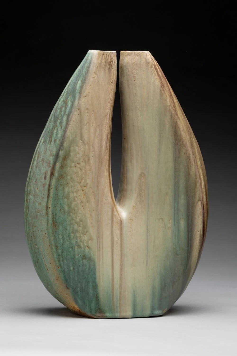 Abstract ceramic sculpture with a rounded, organic shape, glazed in shades of green, beige, and brown.