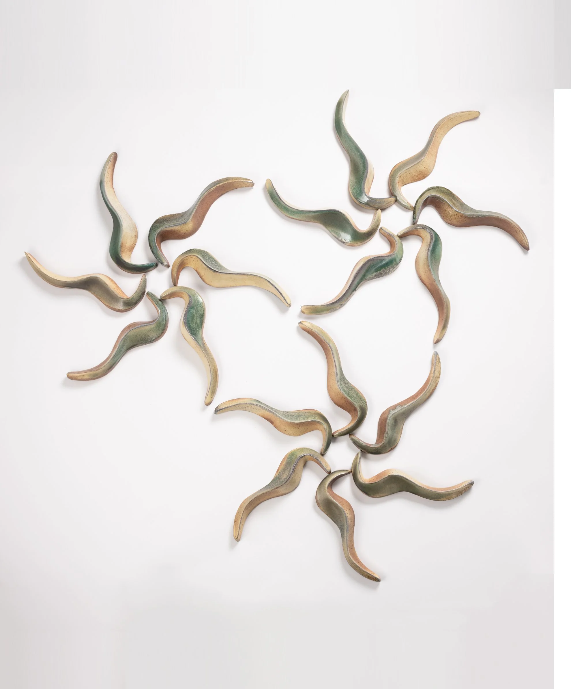 A wall installation made up of 18 curved, elongated ceramic objects with yellow/green surfaces, arranged on a white background.