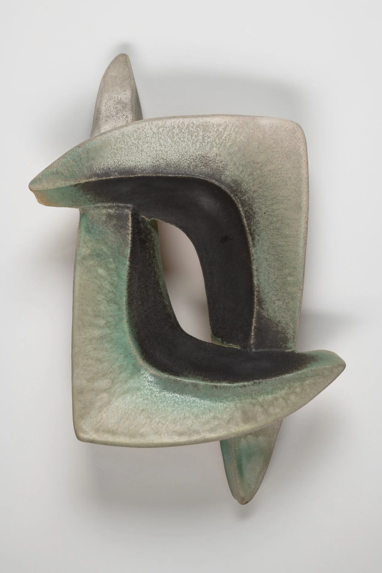 Abstract ceramic sculpture with curved geometric shapes in green, black, and beige tones