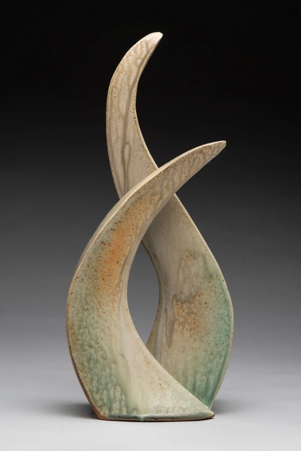 A ceramic sculpture with abstract, curved shapes in muted tones of beige, green, and rust, set against a black background.