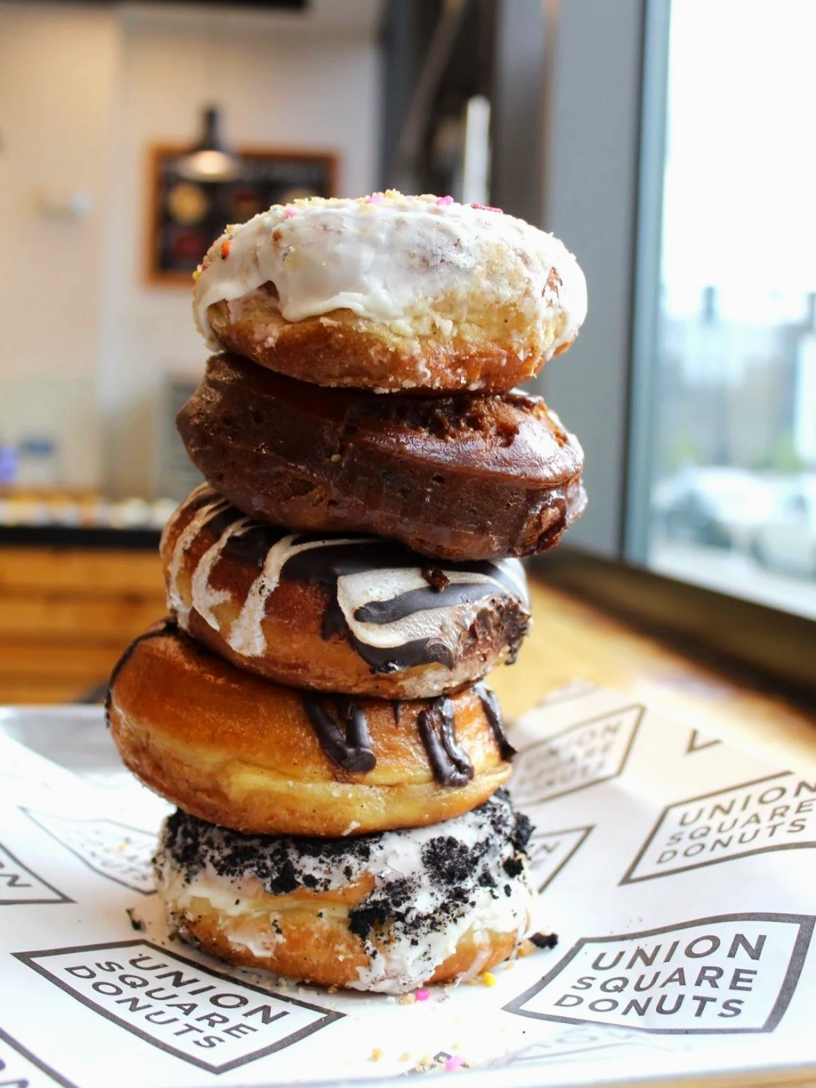 A stack of five assorted donuts on branded parchment paper inside a donut shop.