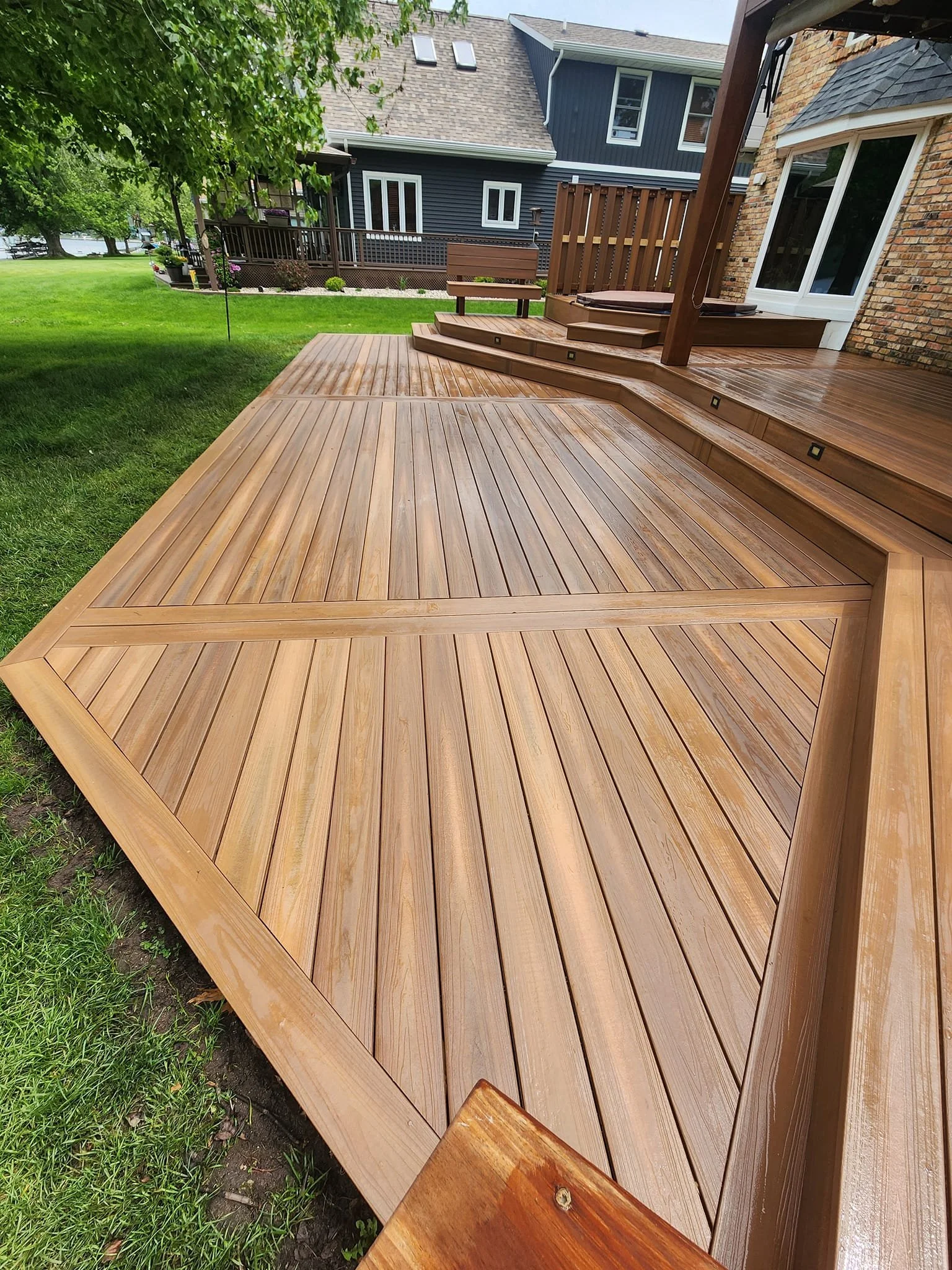 Freshly stained wooden deck with steps leading to a backyard lawn, surrounded by houses and trees.