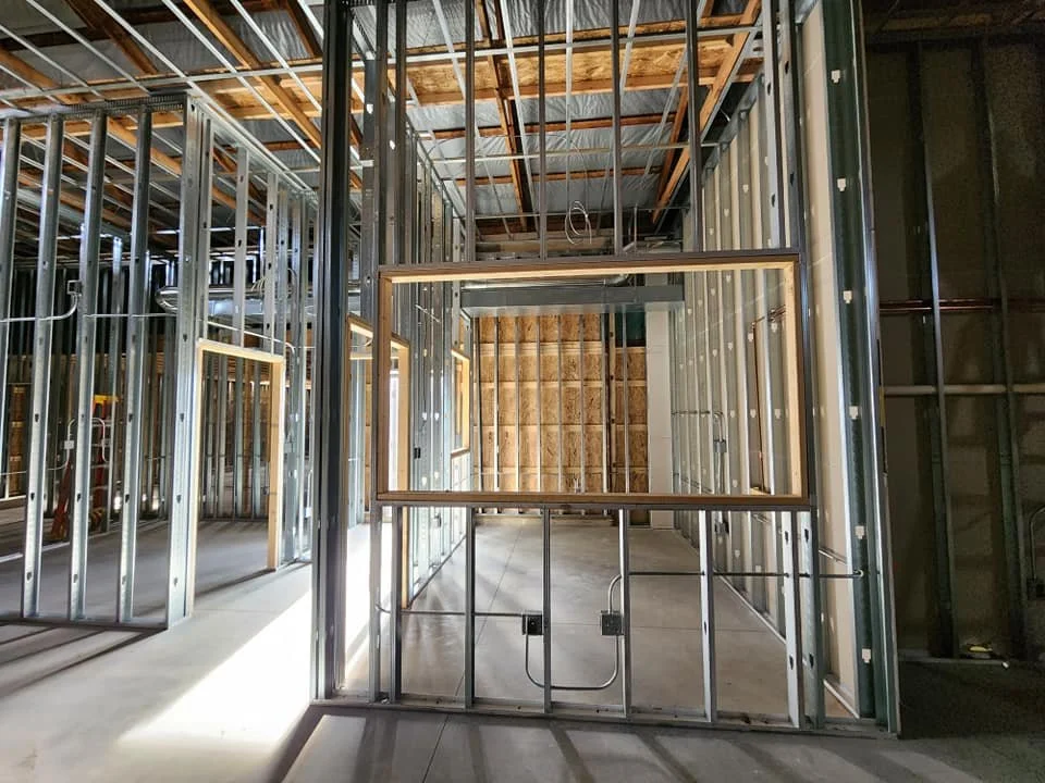Interior of a house under construction showing metal framing, windows, and unfinished walls.