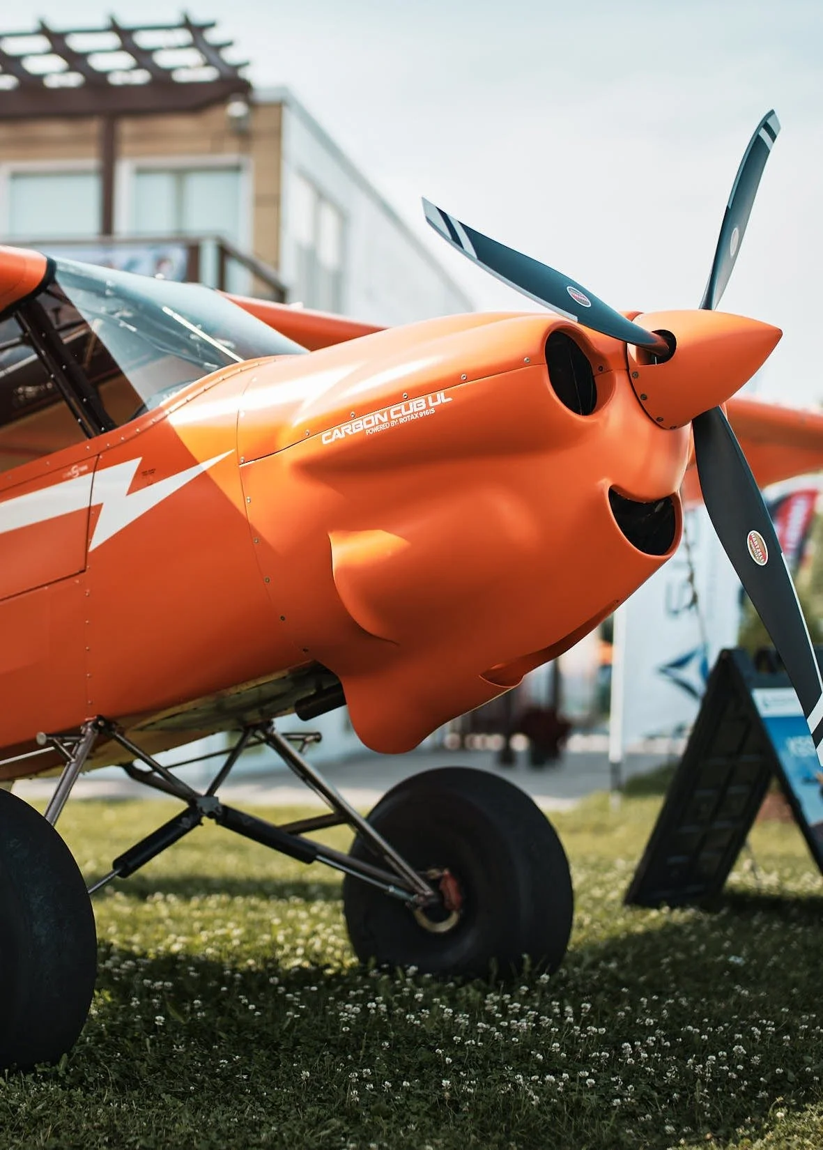 Close-up of an orange carbon fiber aircraft with a propeller, displayed outdoors on grass.