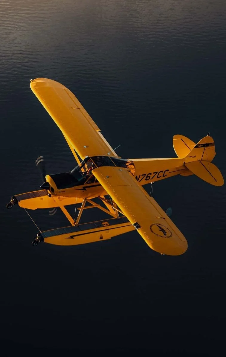 Yellow seaplane flying over water at sunset