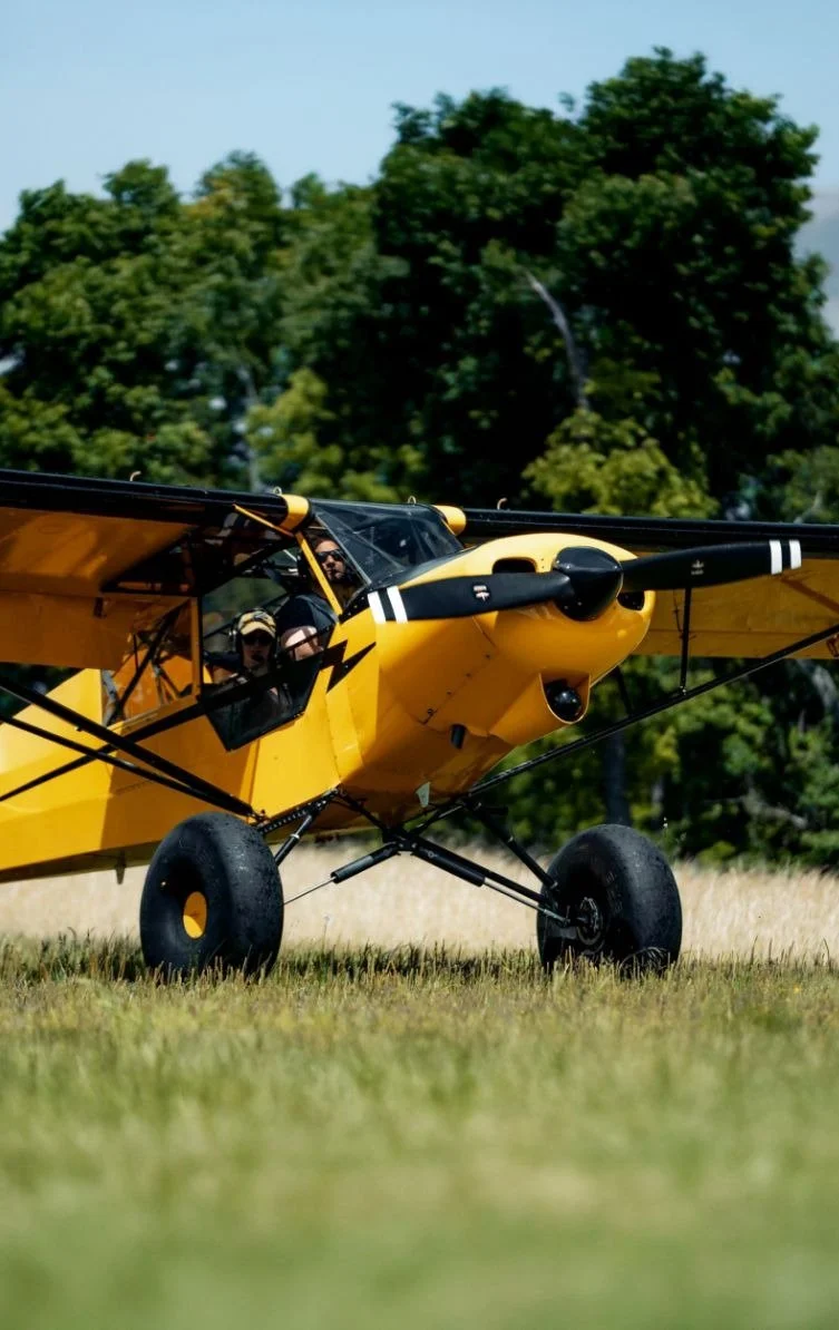 Yellow crop-duster airplane on a grassy field with trees in the background.