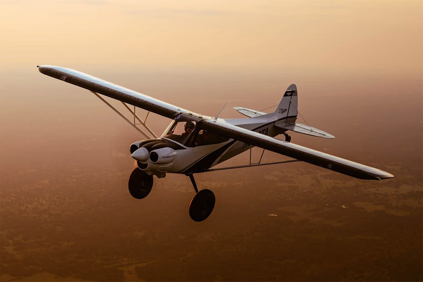 Small aircraft flying during sunset with a desert landscape below.