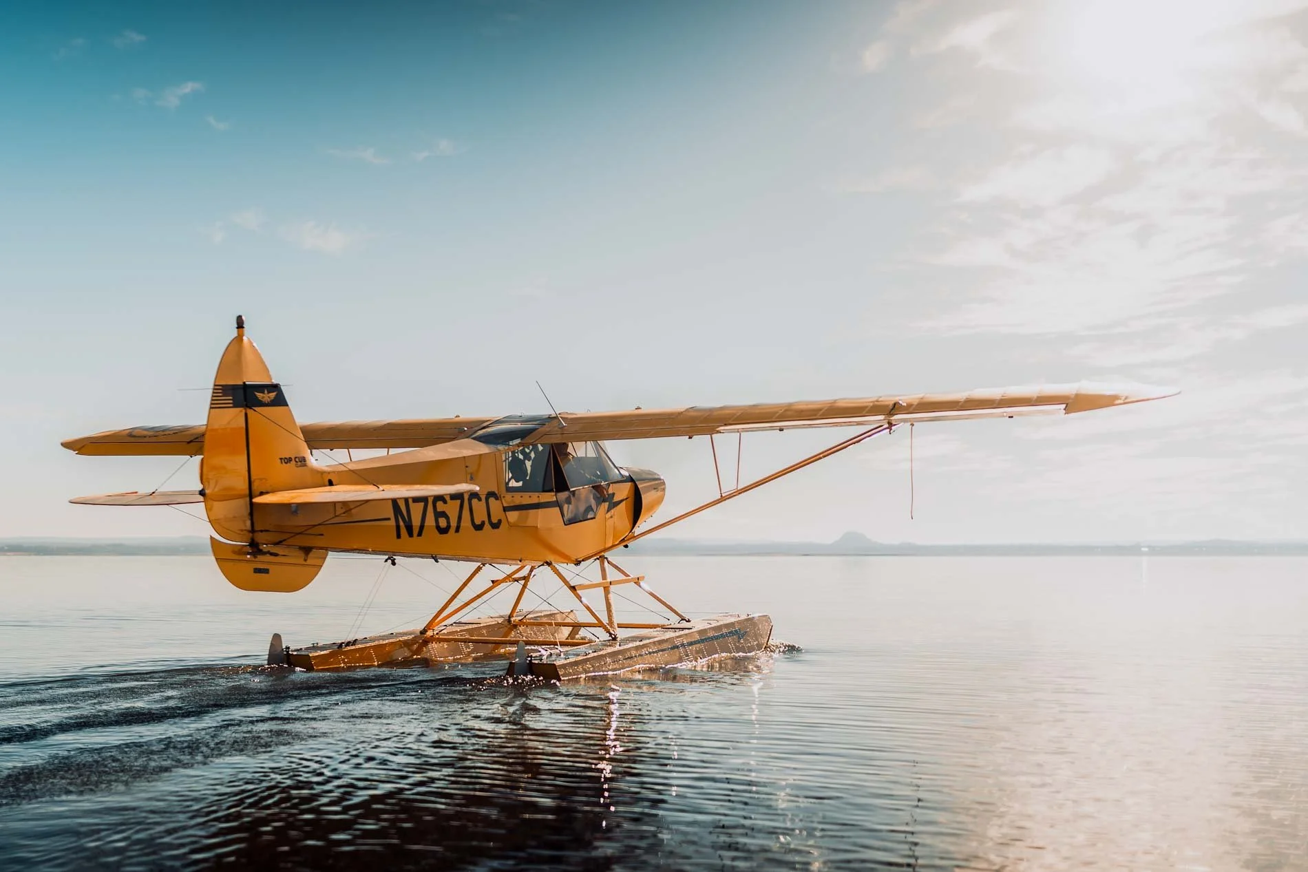 A yellow seaplane on calm water during daytime with a partly cloudy sky.