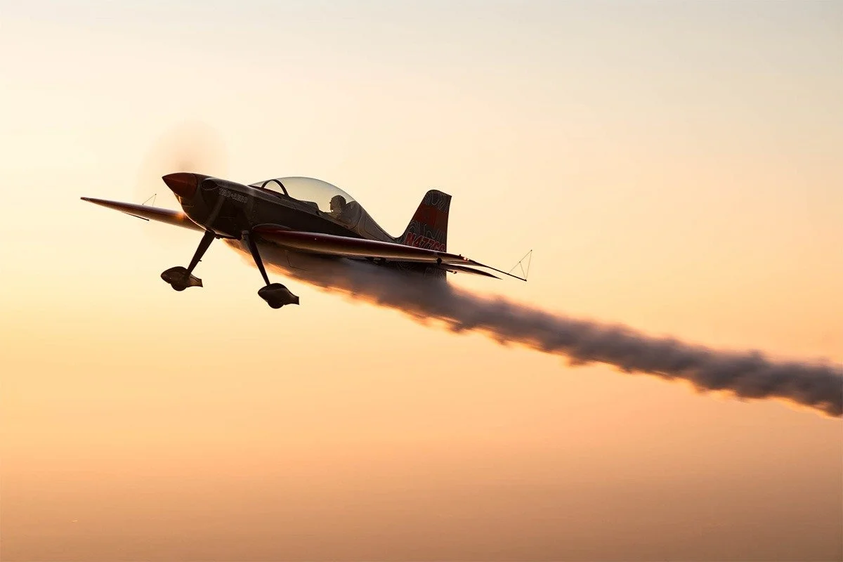 A small jet aircraft flying at sunset with smoke coming from its engines.