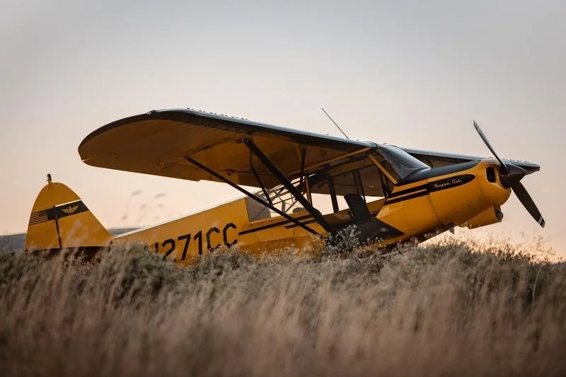 Yellow single-engine propeller plane on grassy terrain at sunset.