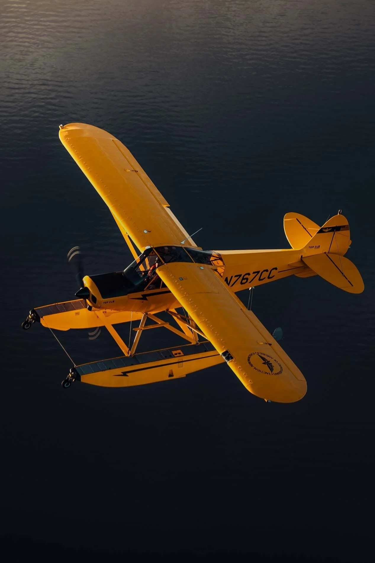 A small yellow seaplane flying over dark ocean water.