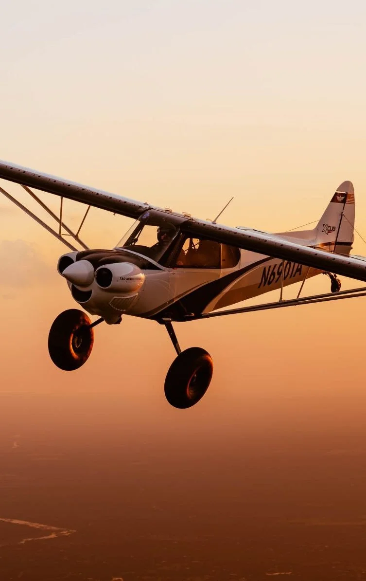 Small propeller airplane flying at sunset with a clear sky and a faint ground below.