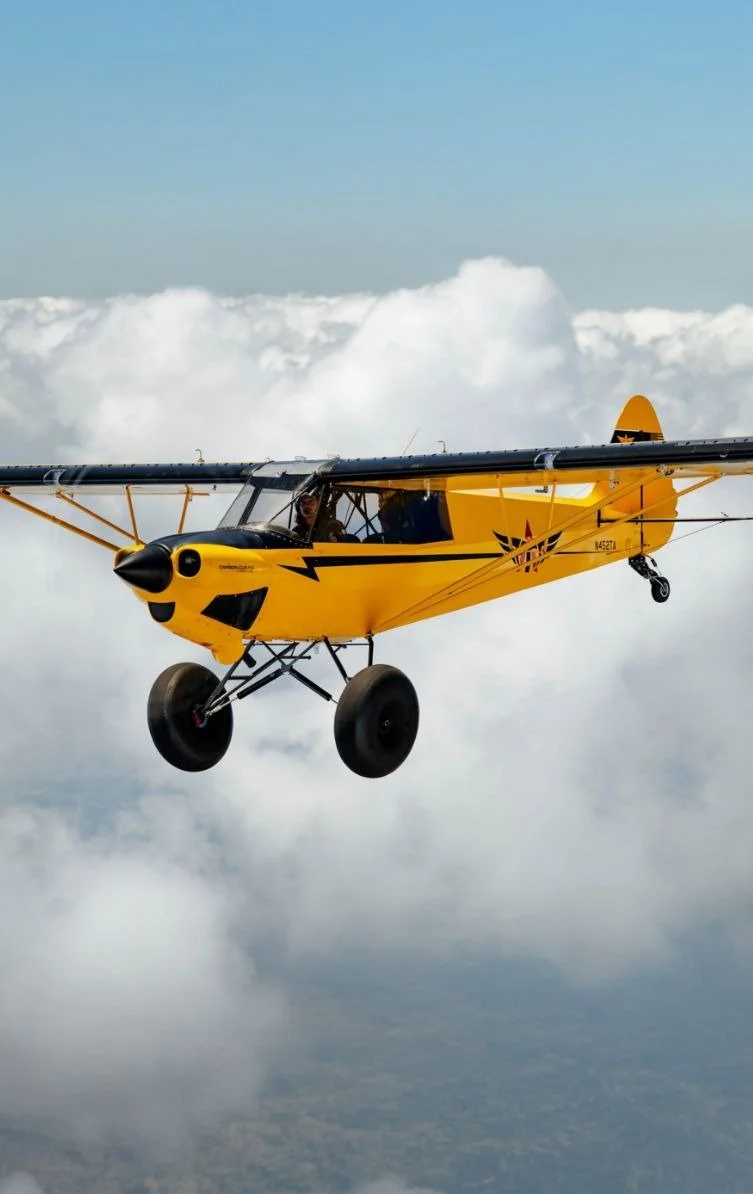 A yellow airplane with black details flying above the clouds.