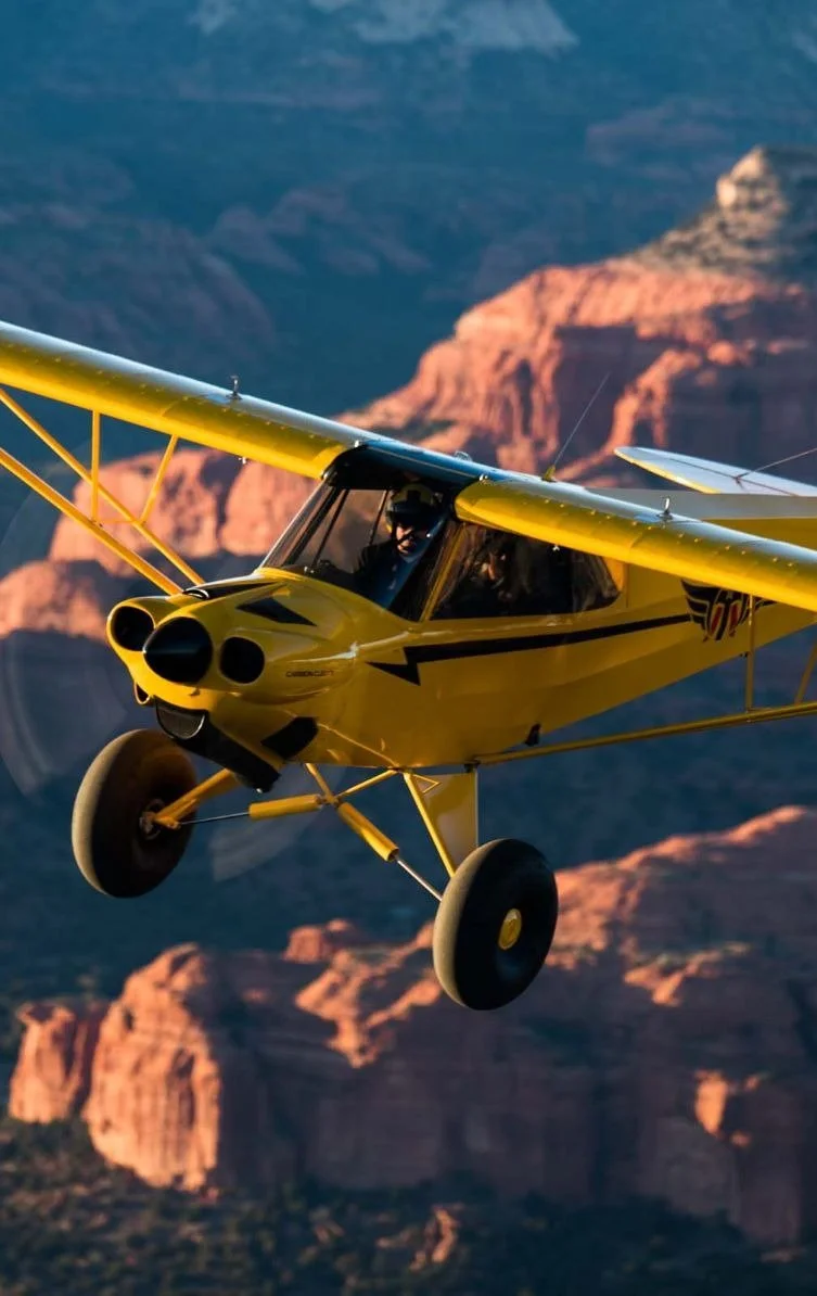 A yellow small airplane flying over the Grand Canyon with red rock formations visible below.