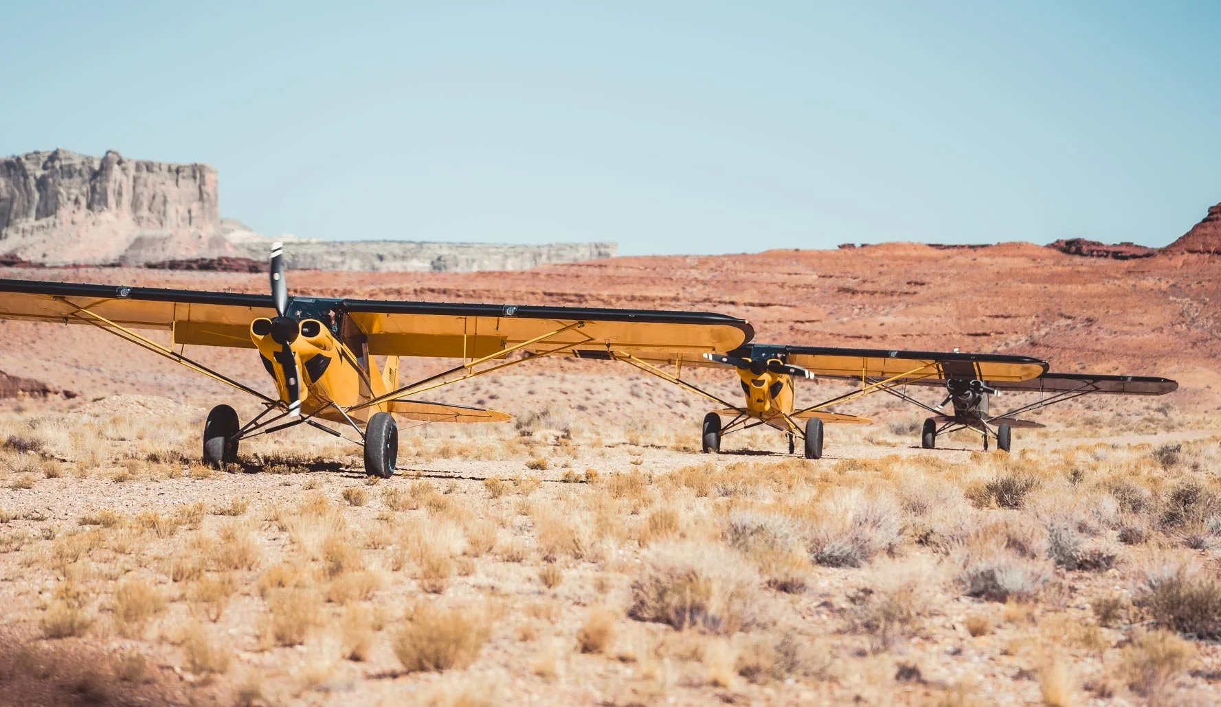 Three small yellow and black aircrafts parked on a dry desert landscape with red rock formations in the background.