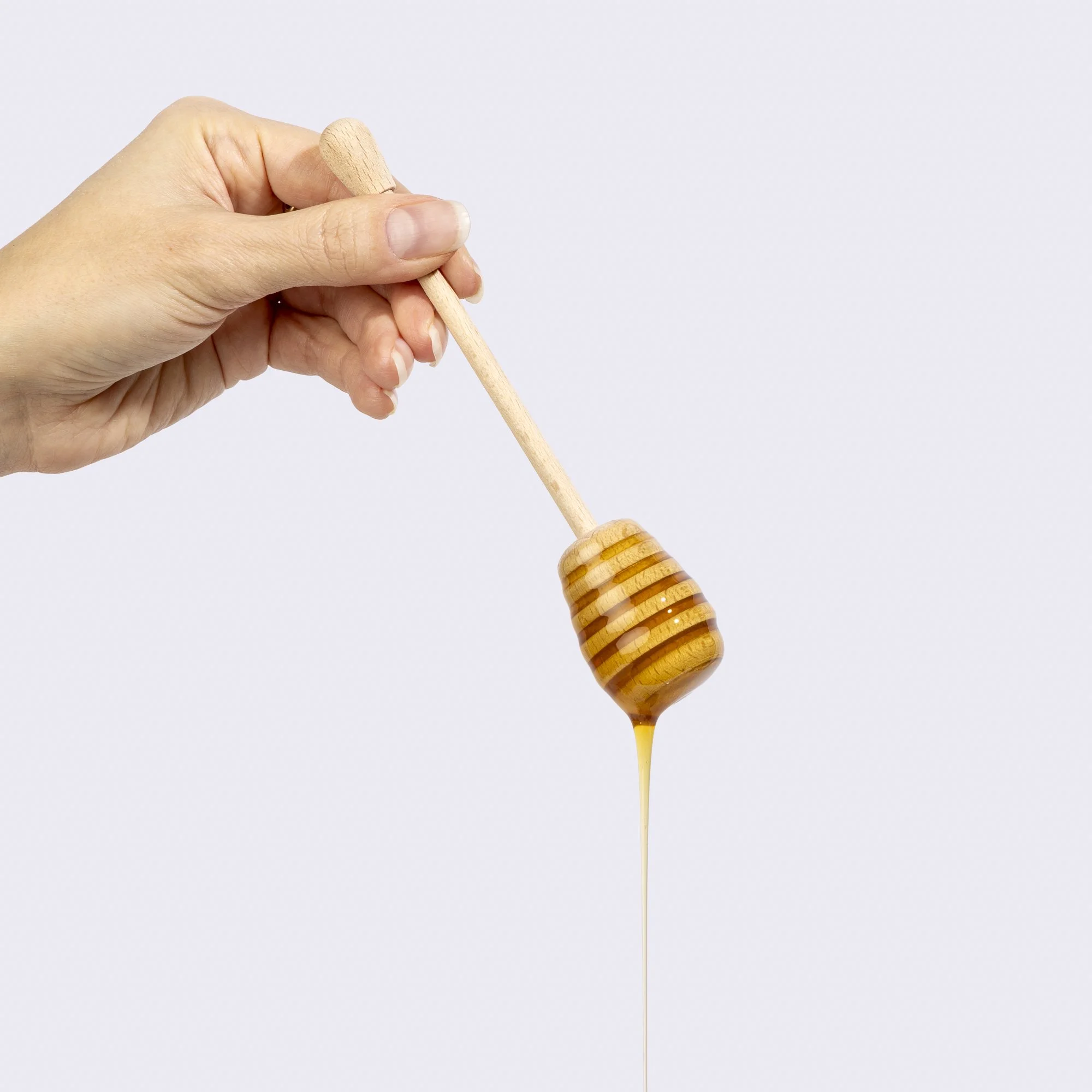 A hand holding a honey dipper with golden honey dripping from it against a plain white background.