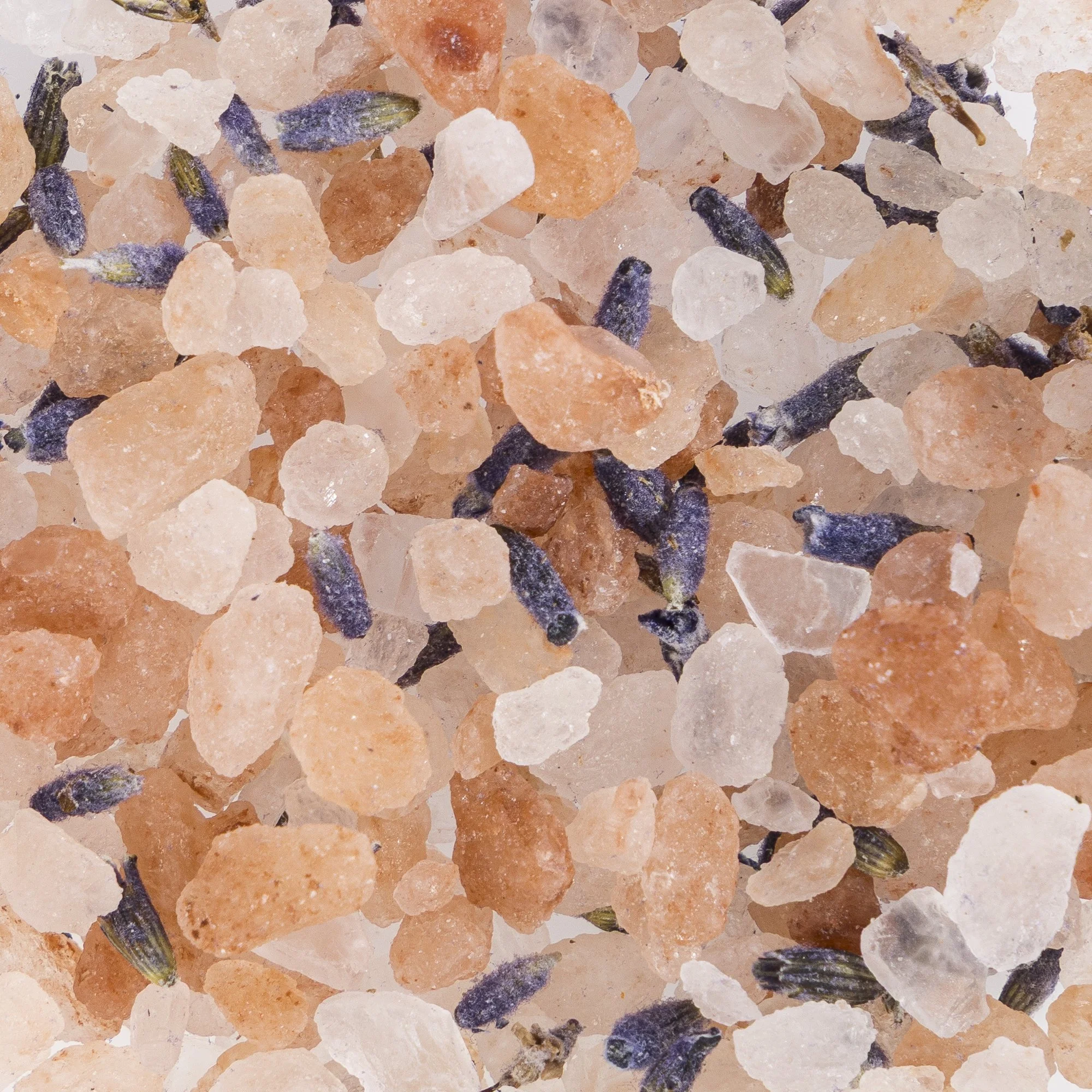 Close-up view of a mixture of pink Himalayan salt crystals with small lavender buds and dark herbs scattered throughout.