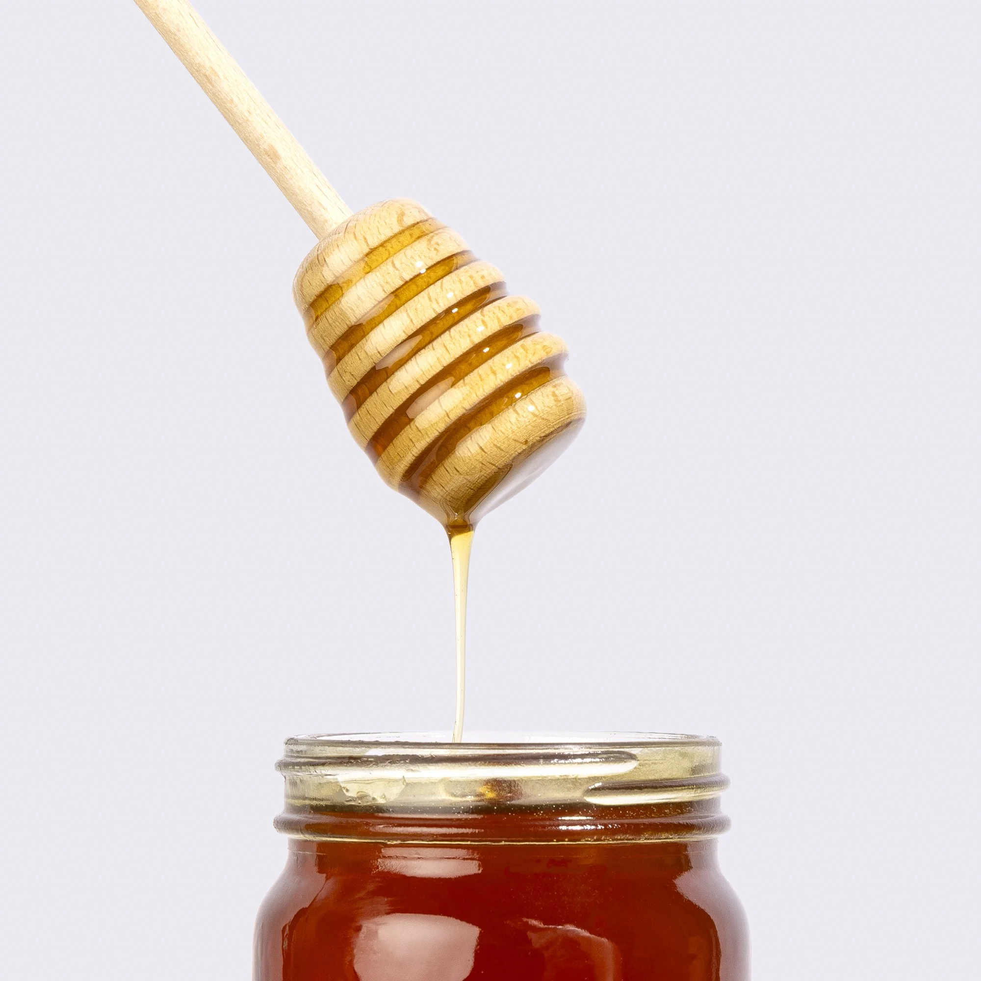 Close-up of honey being poured from a honey dipper into a jar.