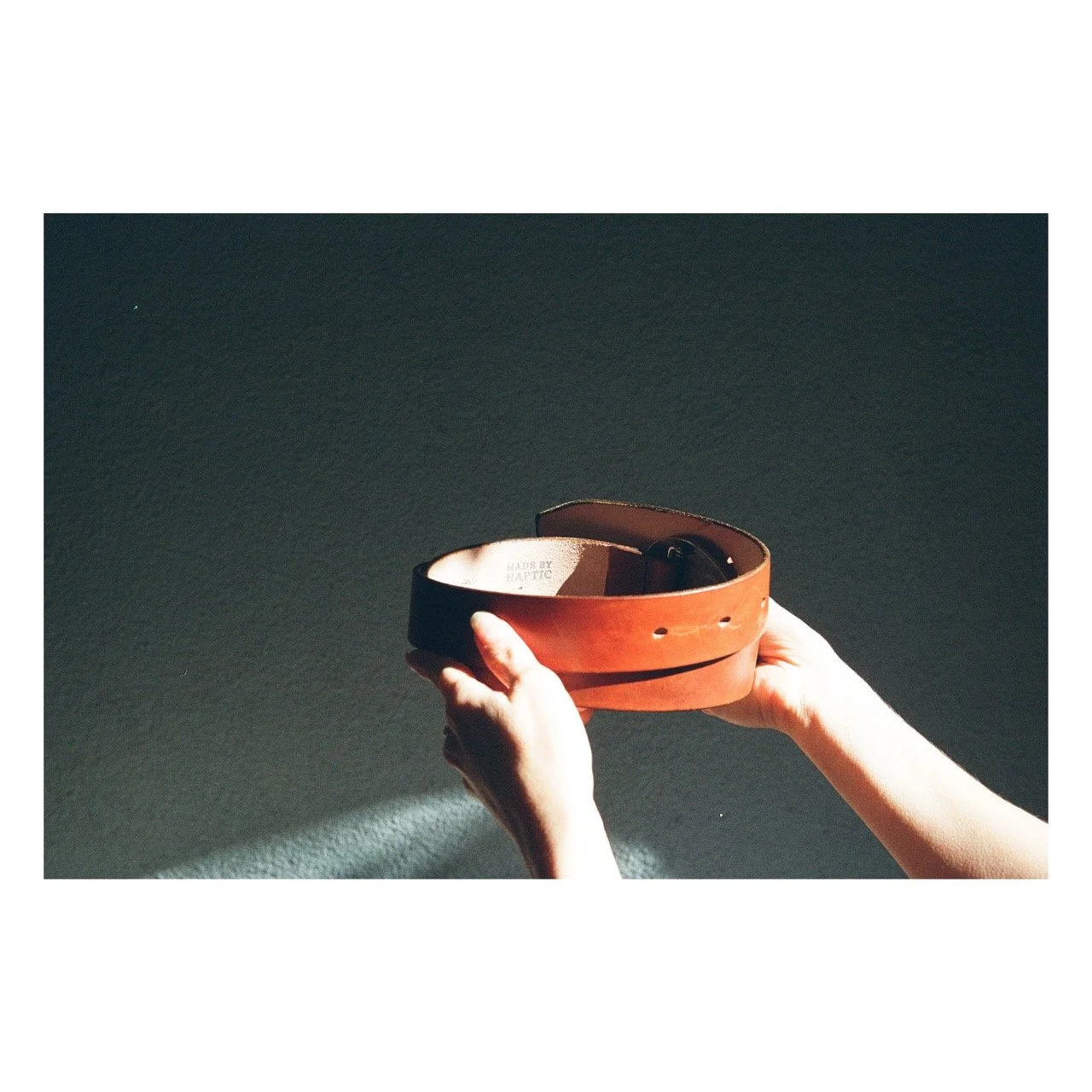 Two hands holding a brown leather belt against a dark background.