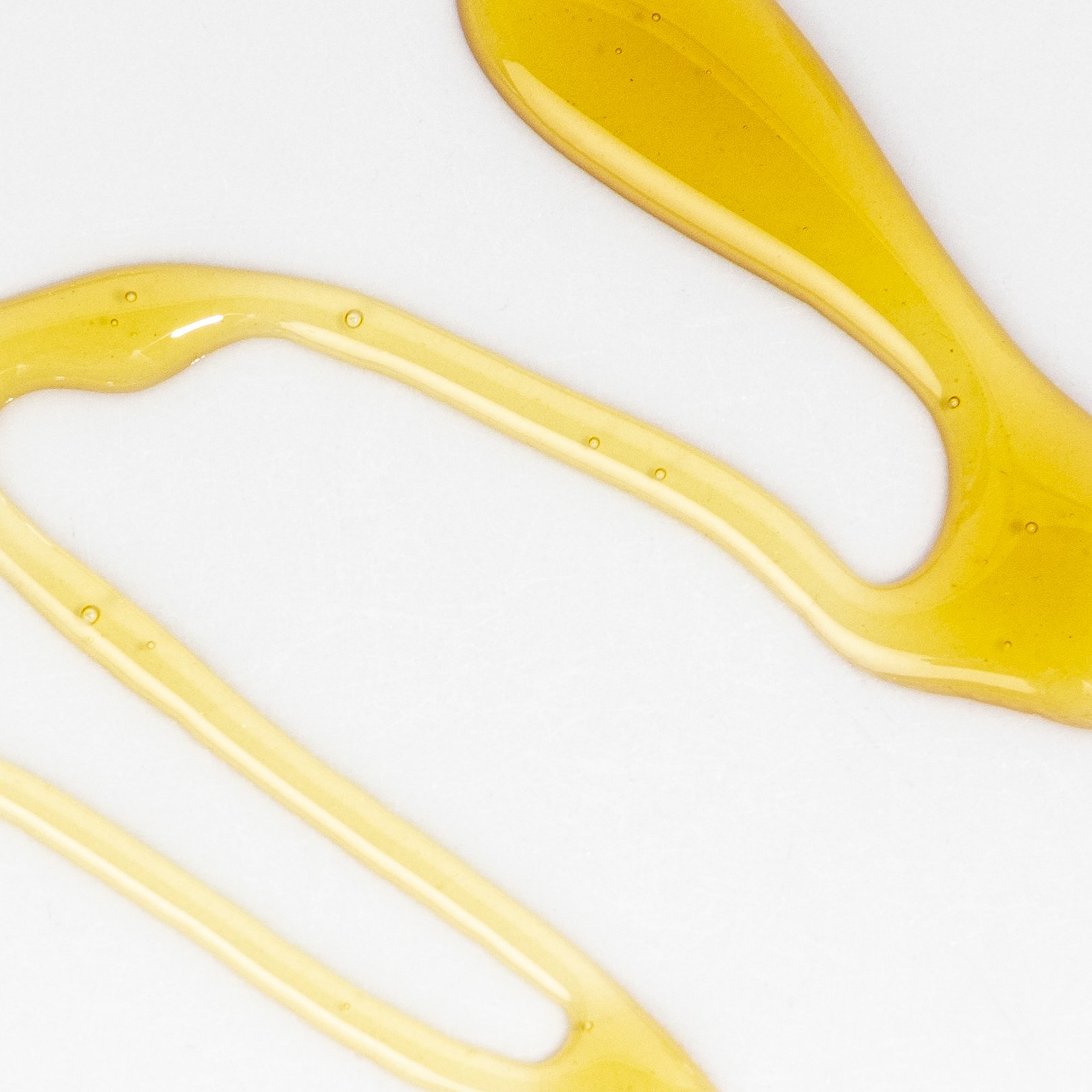 Close-up of yellow honey drizzle on a white surface.