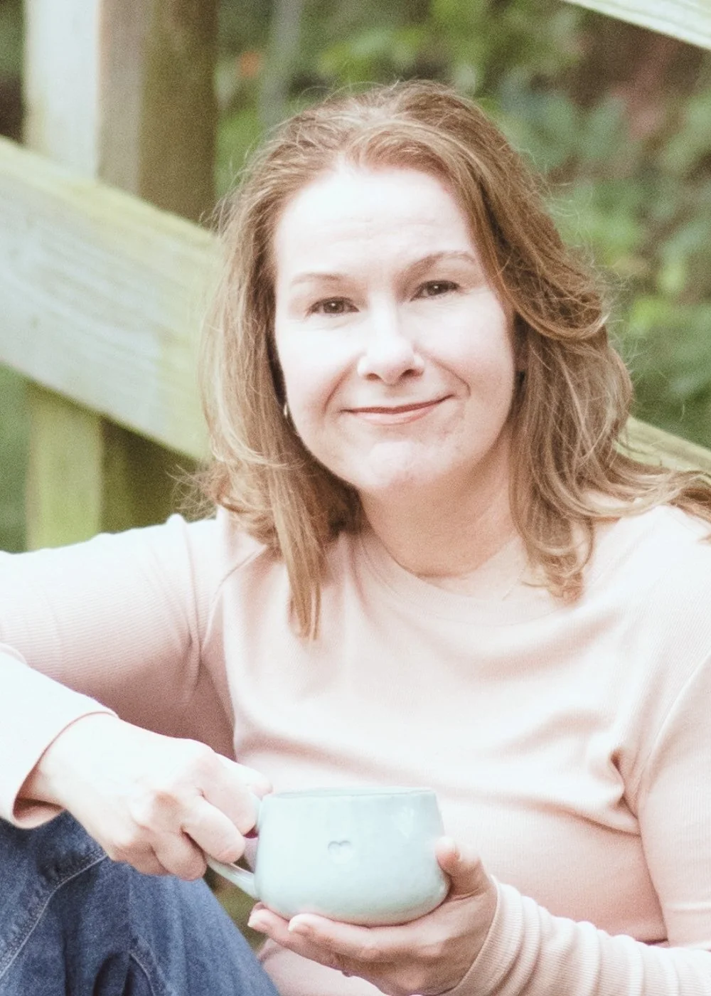 Shannon Champion, Kingwood therapist with light brown hair smiling while holding a coffee mug outdoors near a wooden railing.