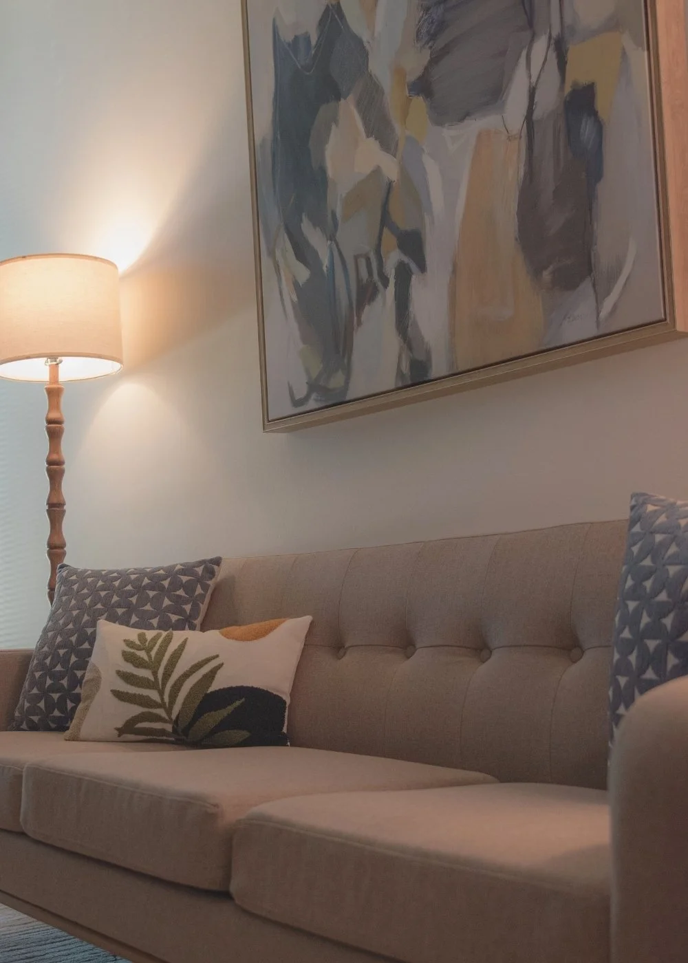 Therapy office with beige couch, decorative pillows, abstract wall art, and soft lamp lighting.