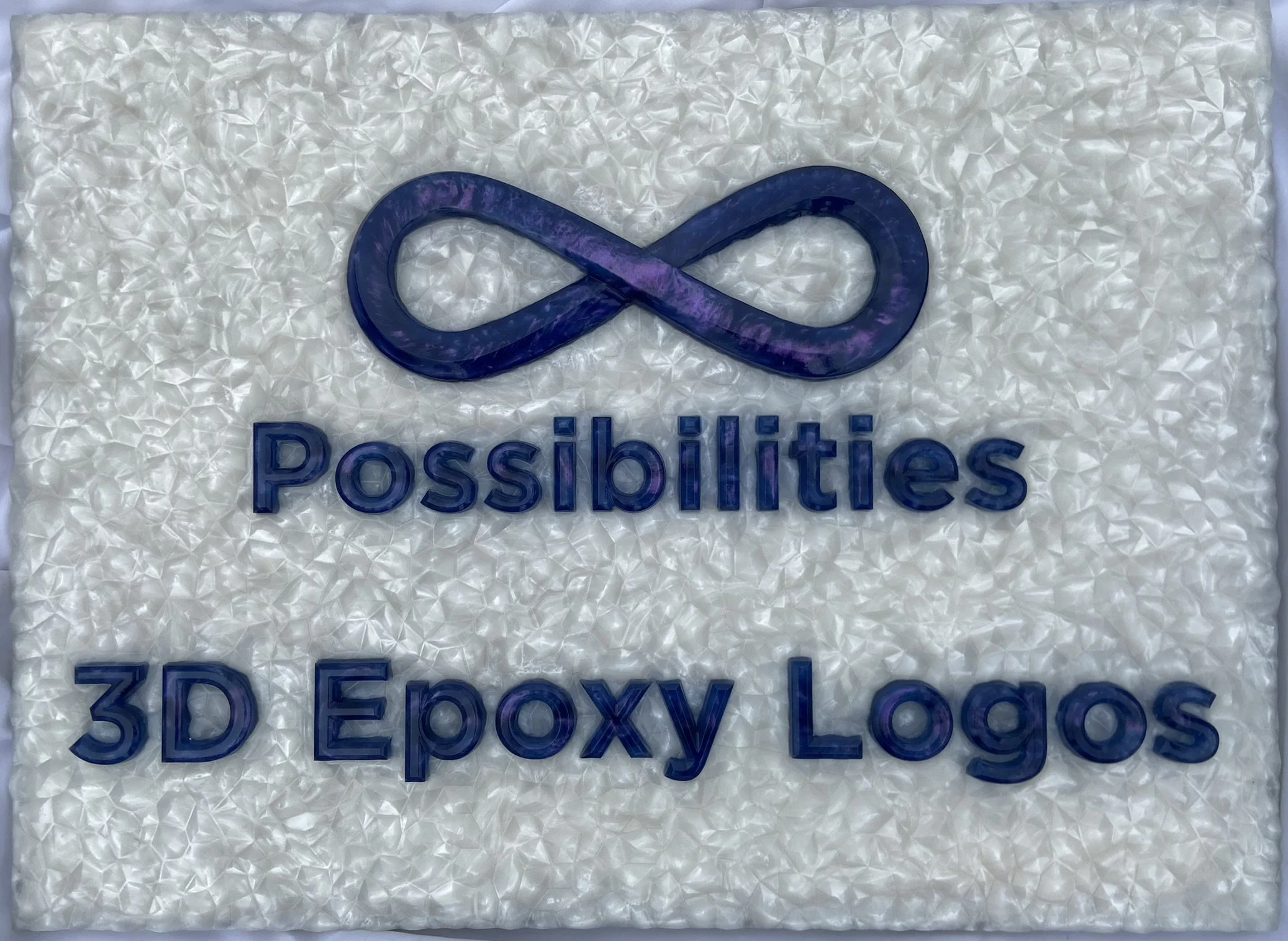 A 3D epoxy logo with text that displays "Infinite Possibilities 3D Epoxy Logos". The letters shift colors between purple and blue-green. The background looks like it's made of white crystals in a lattice.