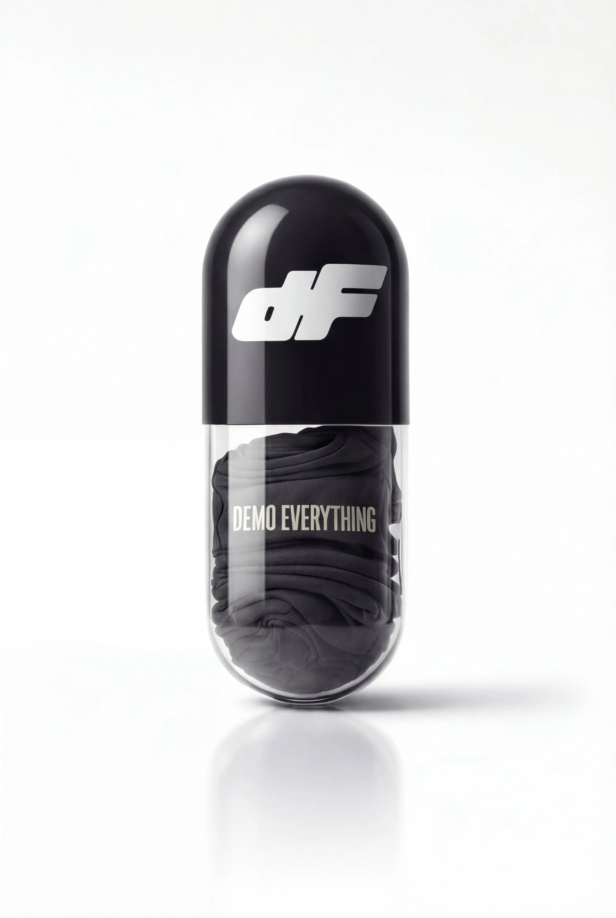 A capsule-shaped container with a black top and transparent body showing black clothing inside. The container has the logo 'dF' on top and the phrase 'DEMO EVERYTHING' printed on the transparent part.