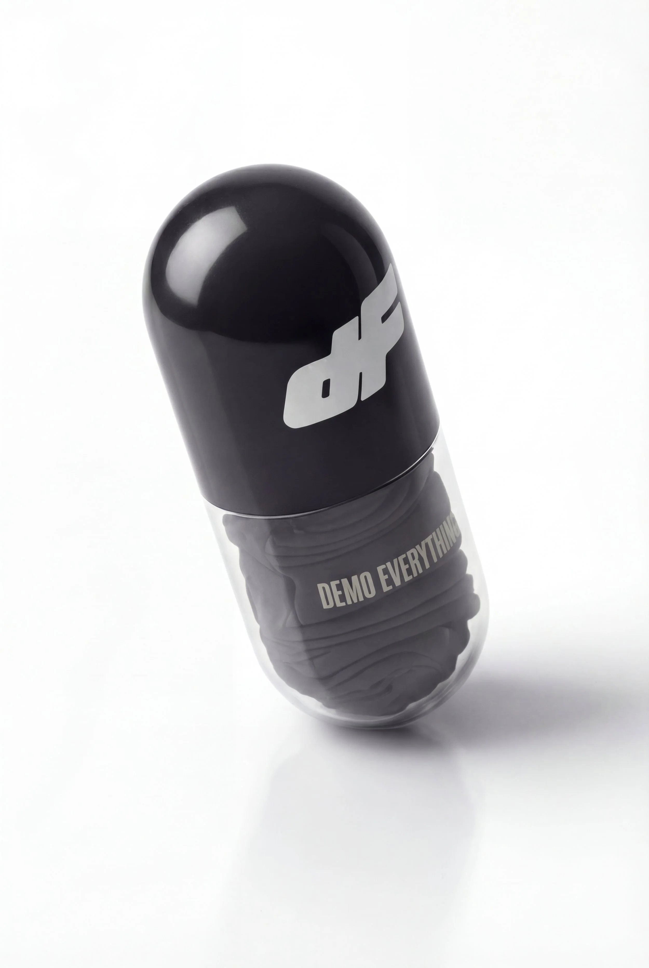 A black pill capsule with the words "DEMO EVERYTHING" on the transparent bottom part and a black top with a white logo.