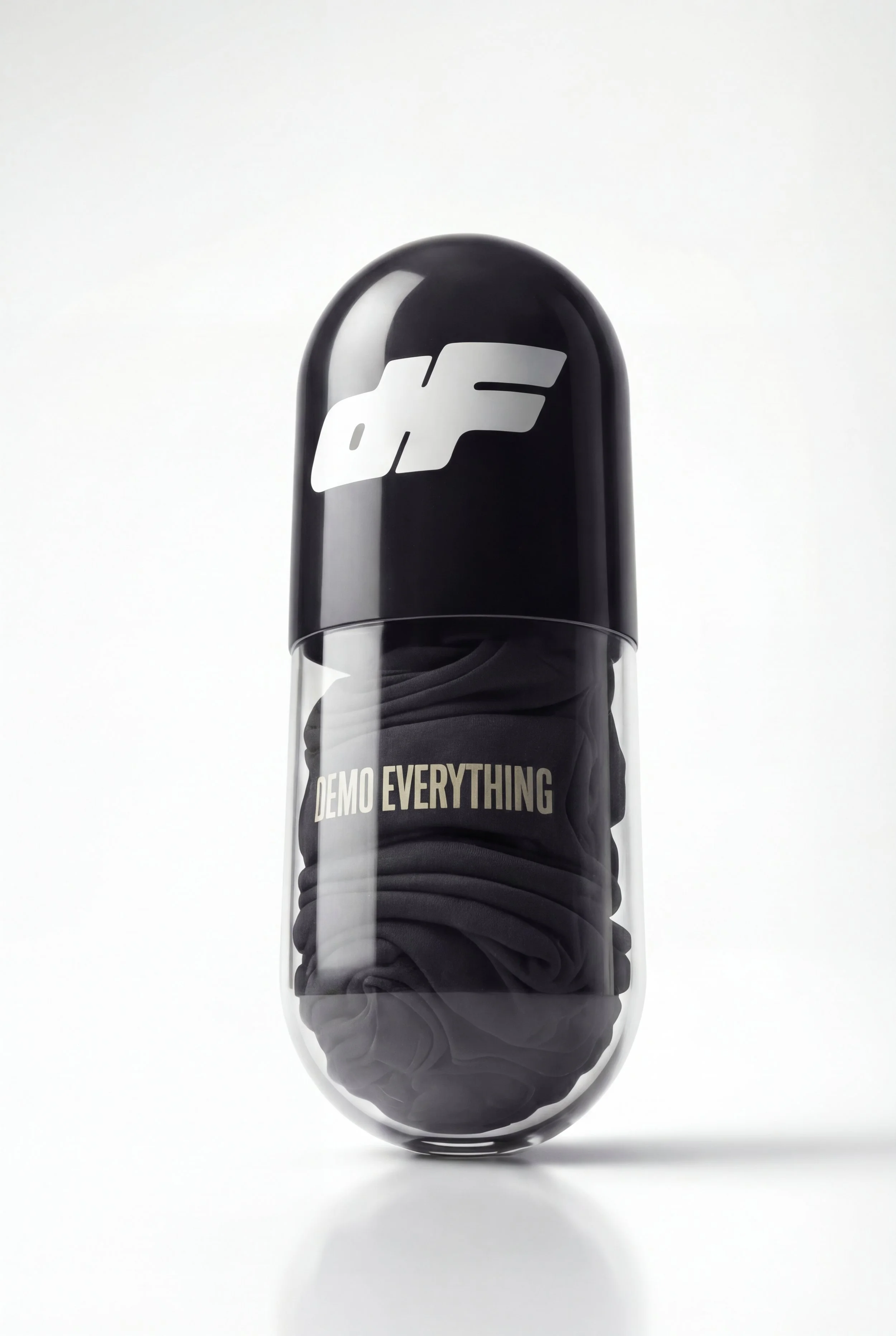 A capsule-shaped container with a black top featuring a white logo, and a clear bottom filled with black fabric with the words "DEMO EVERYTHING" printed on it.
