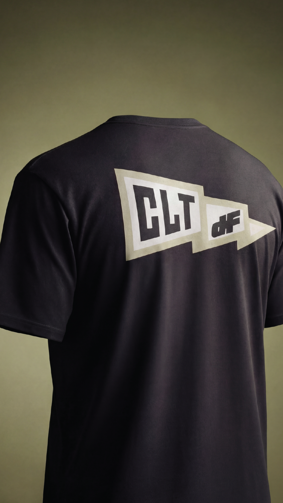 Back of a black DRYFIRE HOUSE T-shirt with the text "CLT" and "of" in white and black, arranged inside a speech bubble pointing to the right.
