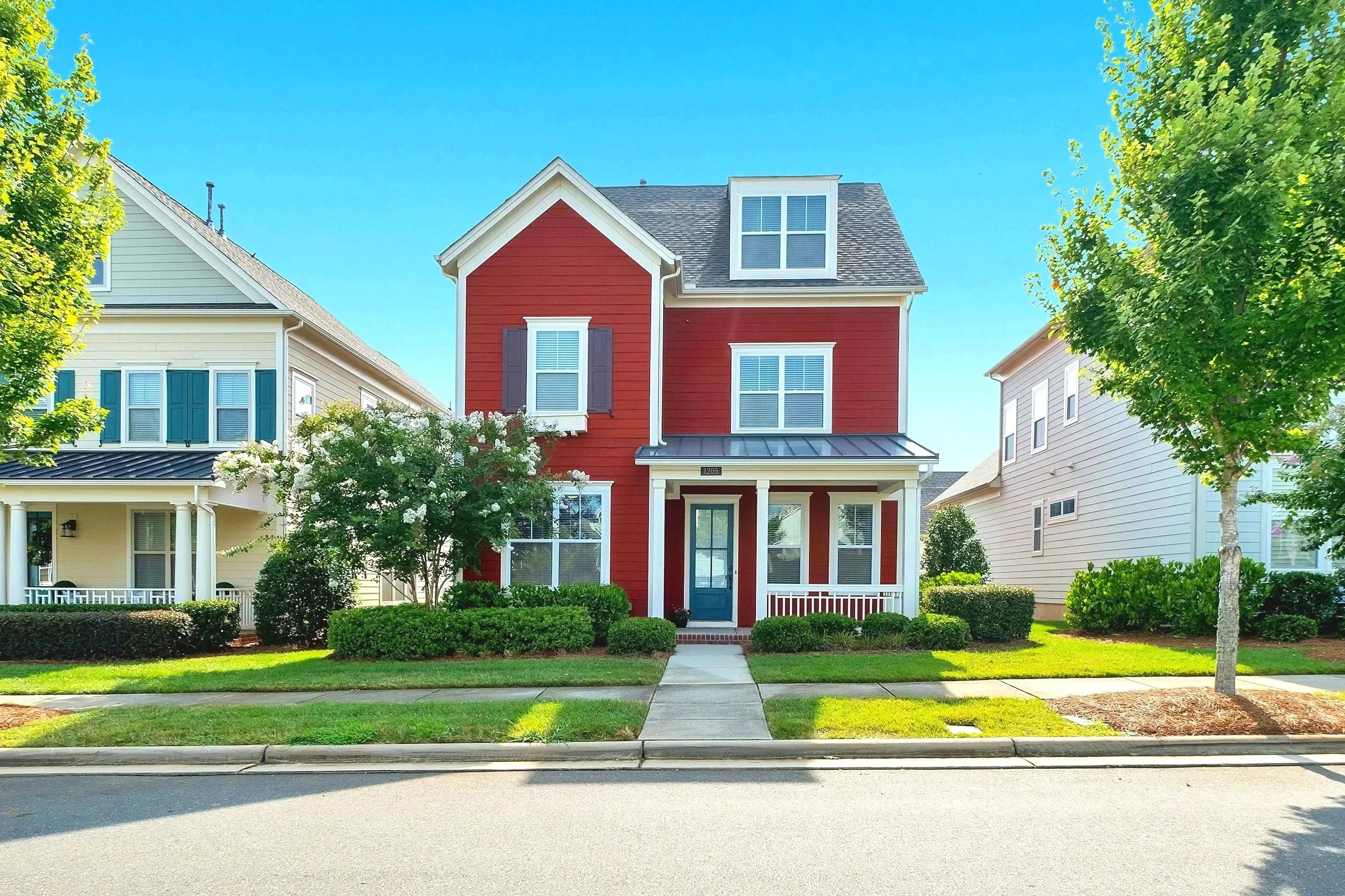 Red three-story house with front porch, front yard, sidewalk, and trees on both sides.