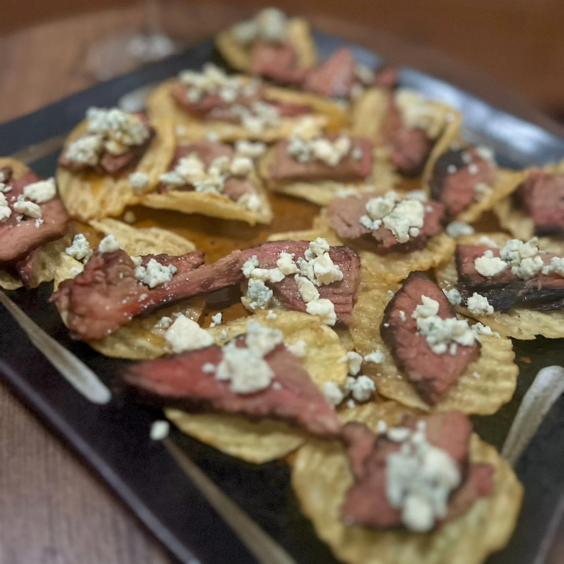 Blue cheese steak chip appetizer plated with a glass of red wine in a restaurant
