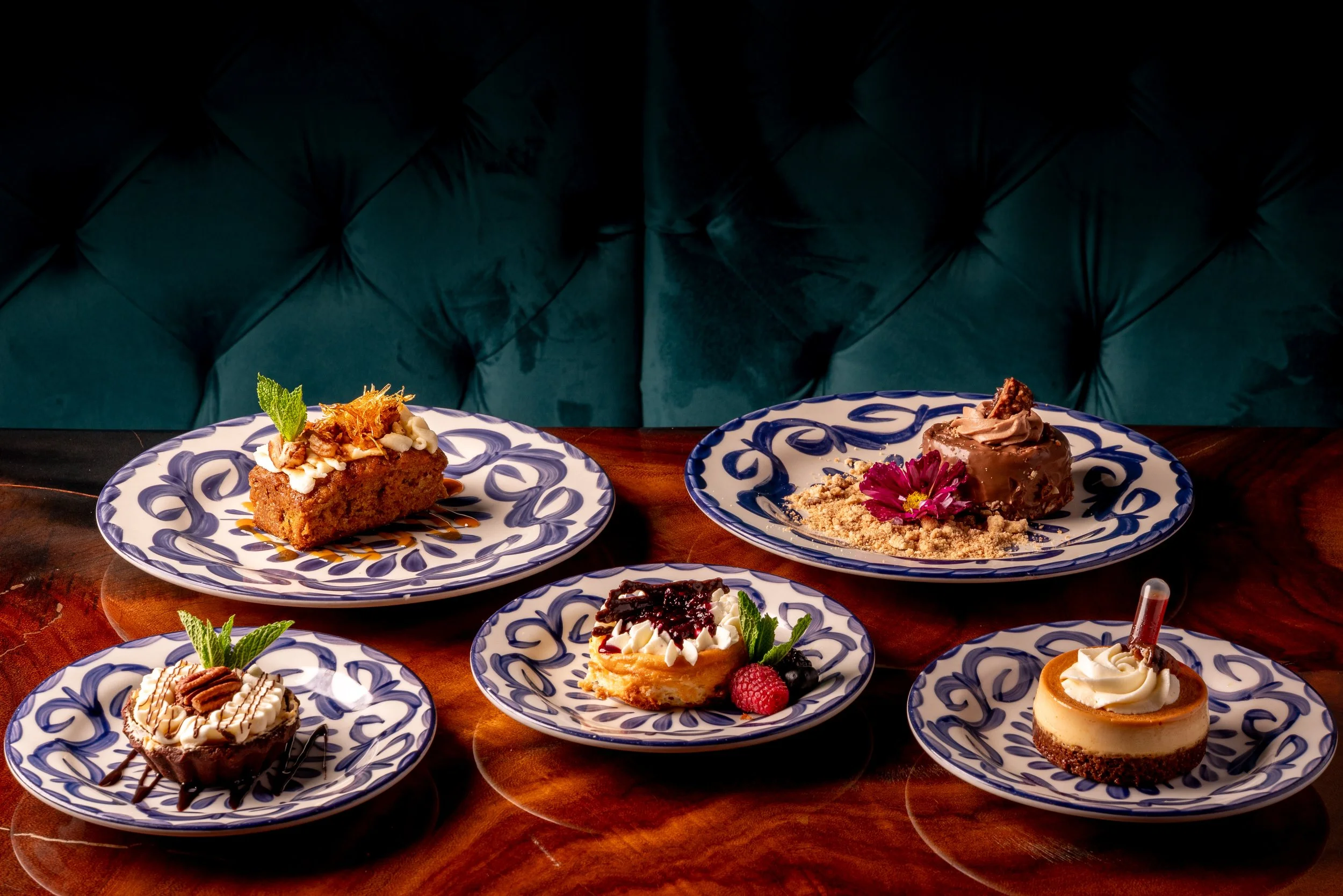 Assorted desserts on blue and white patterned plates, with a dark green tufted background.
