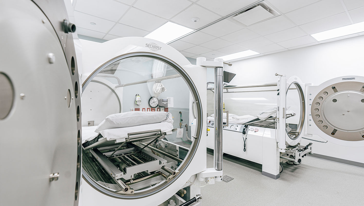 Two MRI machines in a medical examination room, one with a patient bed prepared for a scan.