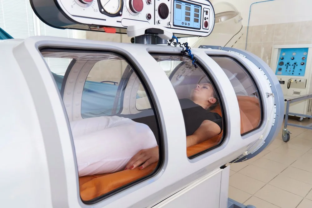 A woman lying inside a hyperbaric oxygen therapy chamber in a medical facility.