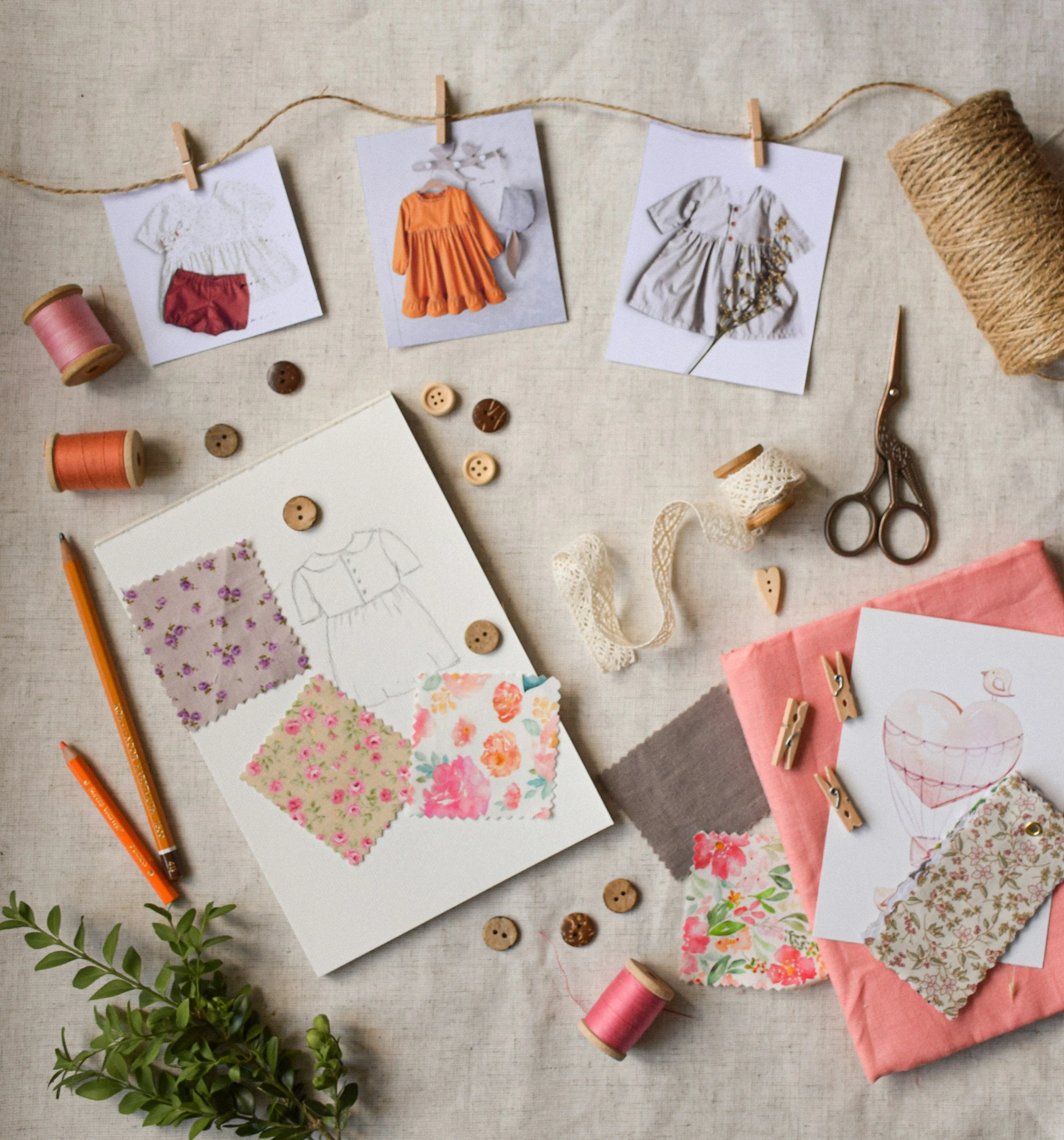 Crafting or sewing workspace with fabric swatches, sketches, buttons, thread, scissors, and fabric photos.