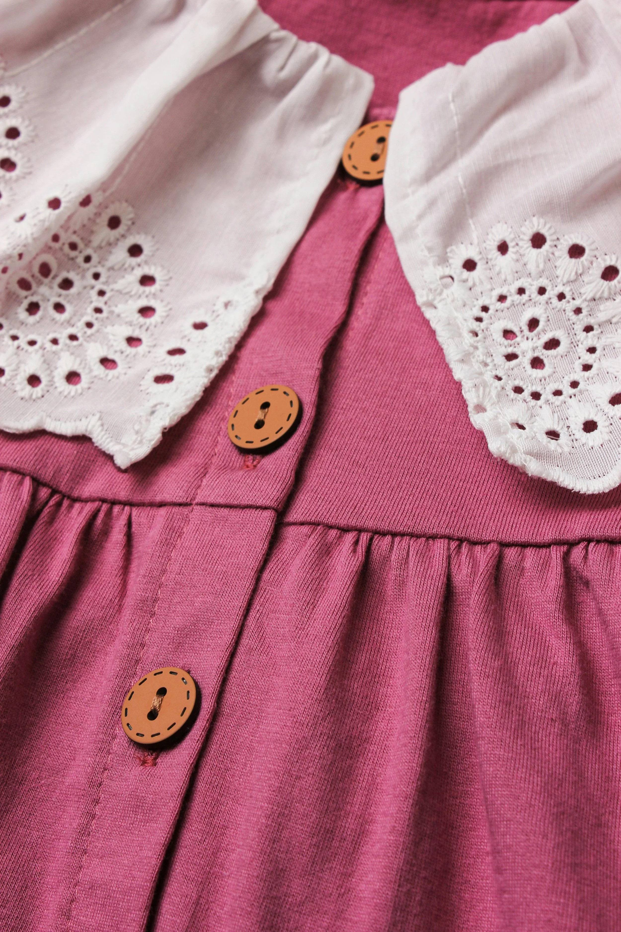 Close-up of a pink dress with a white embroidered collar and brown buttons.