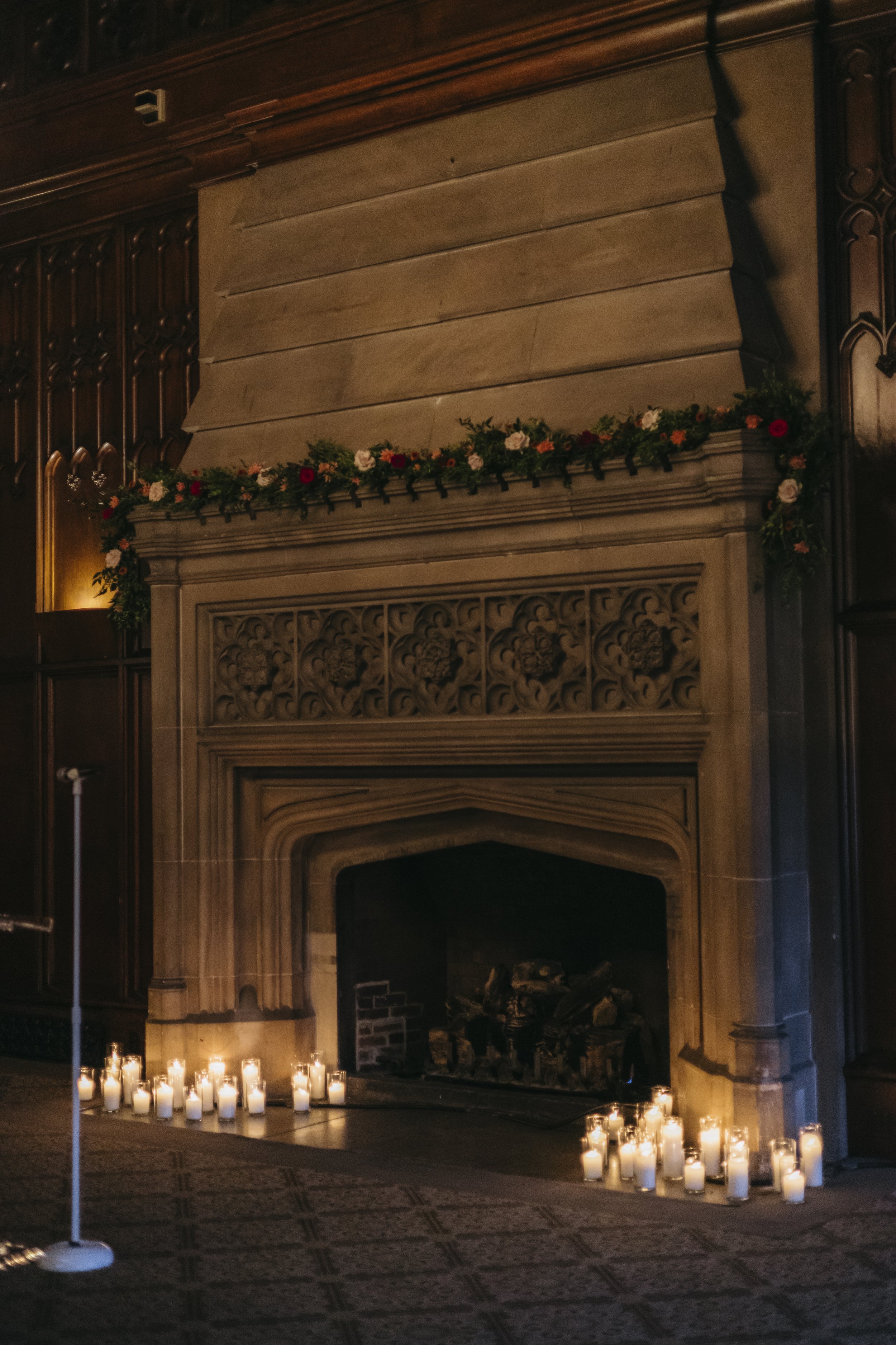 A fireplace decorated with a floral garland and surrounded by candles at the base for a wedding ceremony.