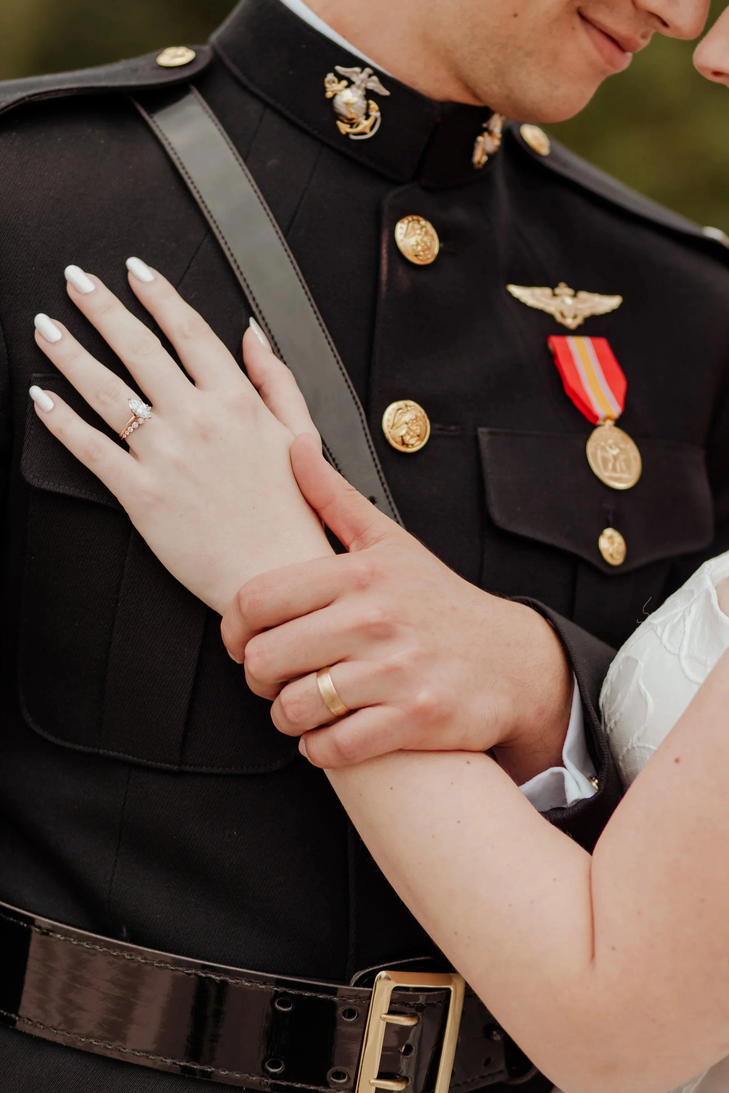 Close-up of a couple in wedding attire, with the groom in military uniform, and the bride displaying her wedding ring.