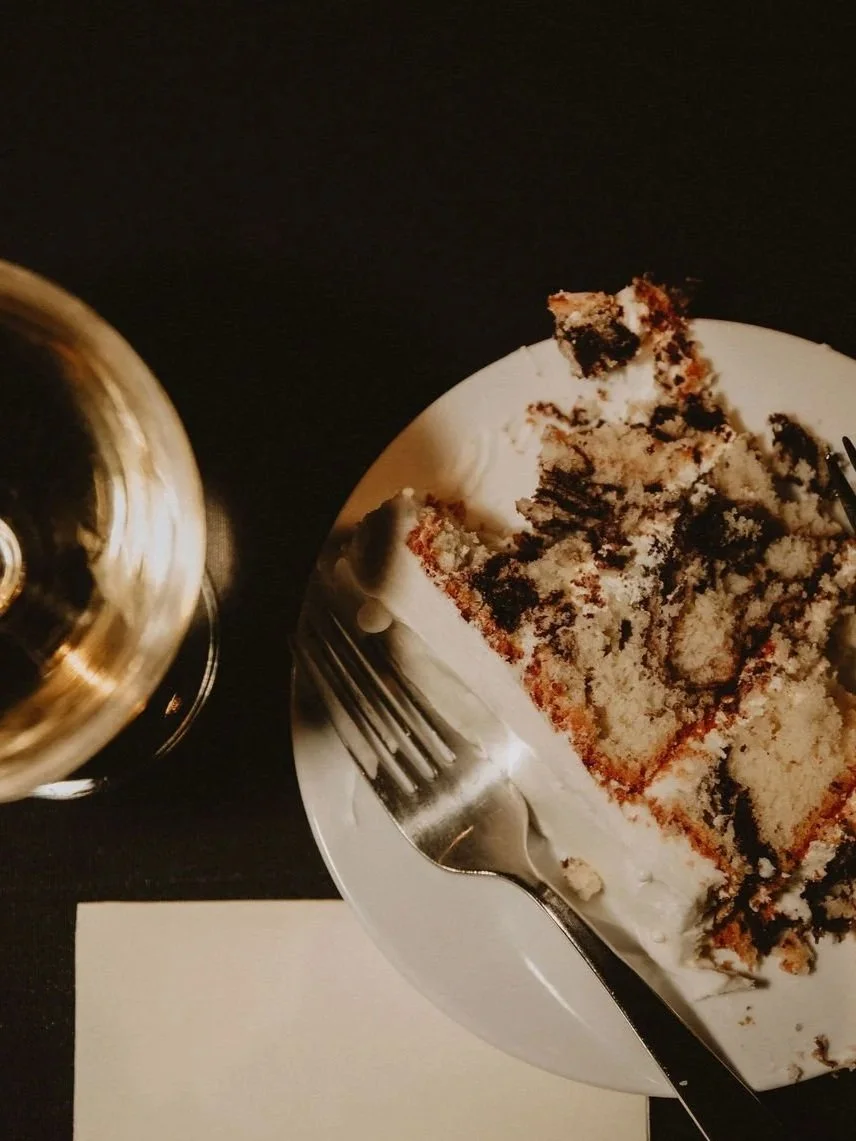 Details shot of the end of a wedding reception featuring a half eaten slice of cake and a half drunk glass of champagne.