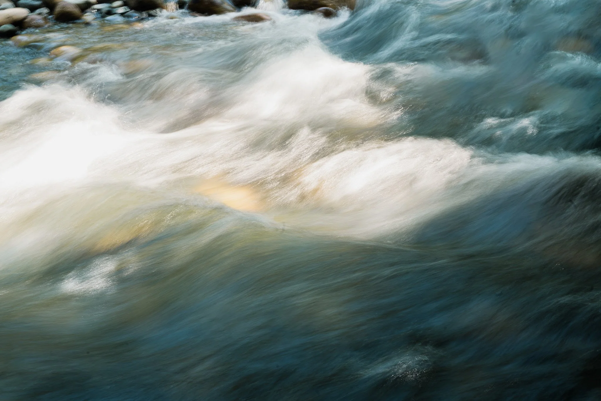 Flowing river water with white foam and rocks visible at the top left.