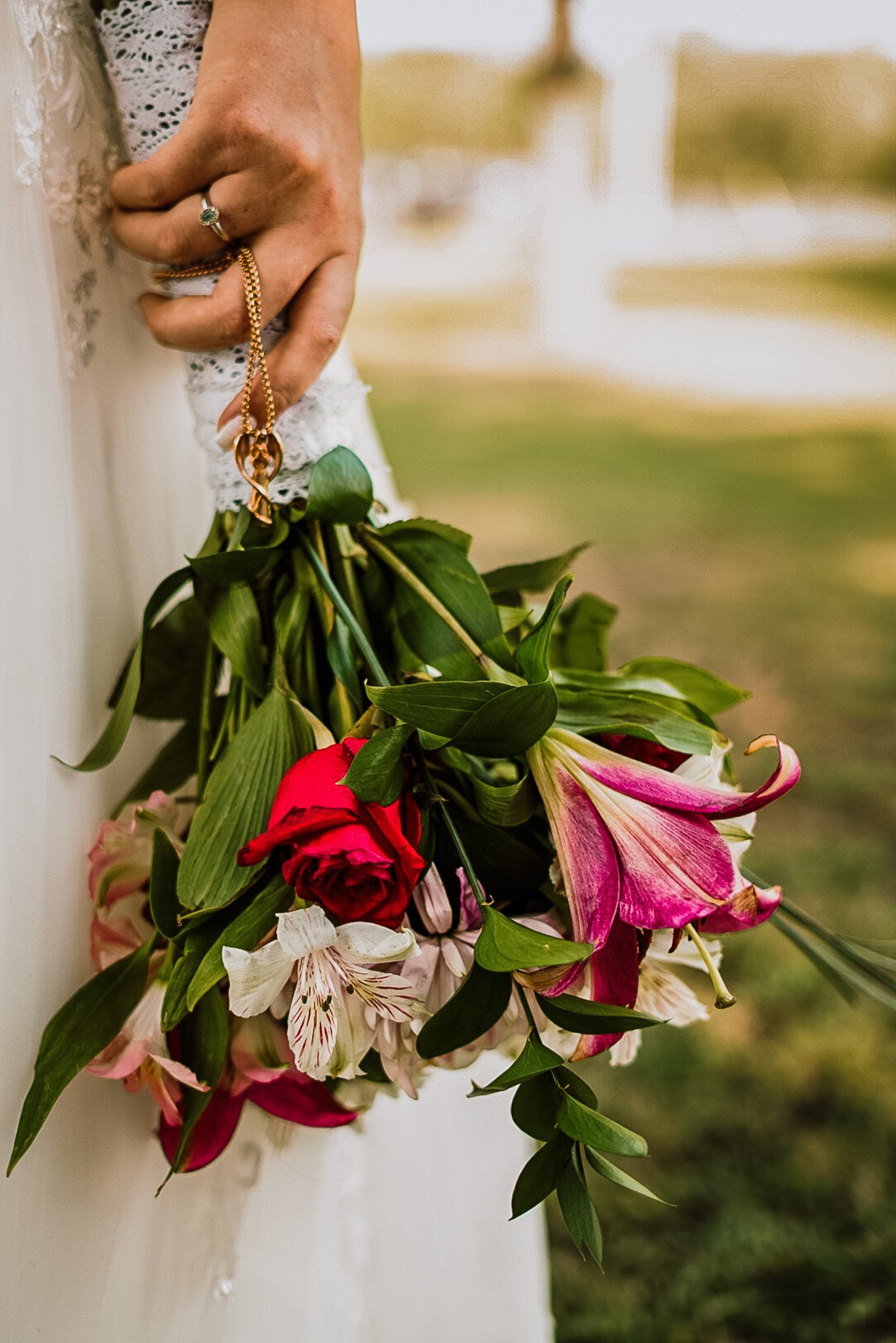 A person in a wedding dress holding a bouquet of pink, white, and red flowers against an outdoor blurred background.