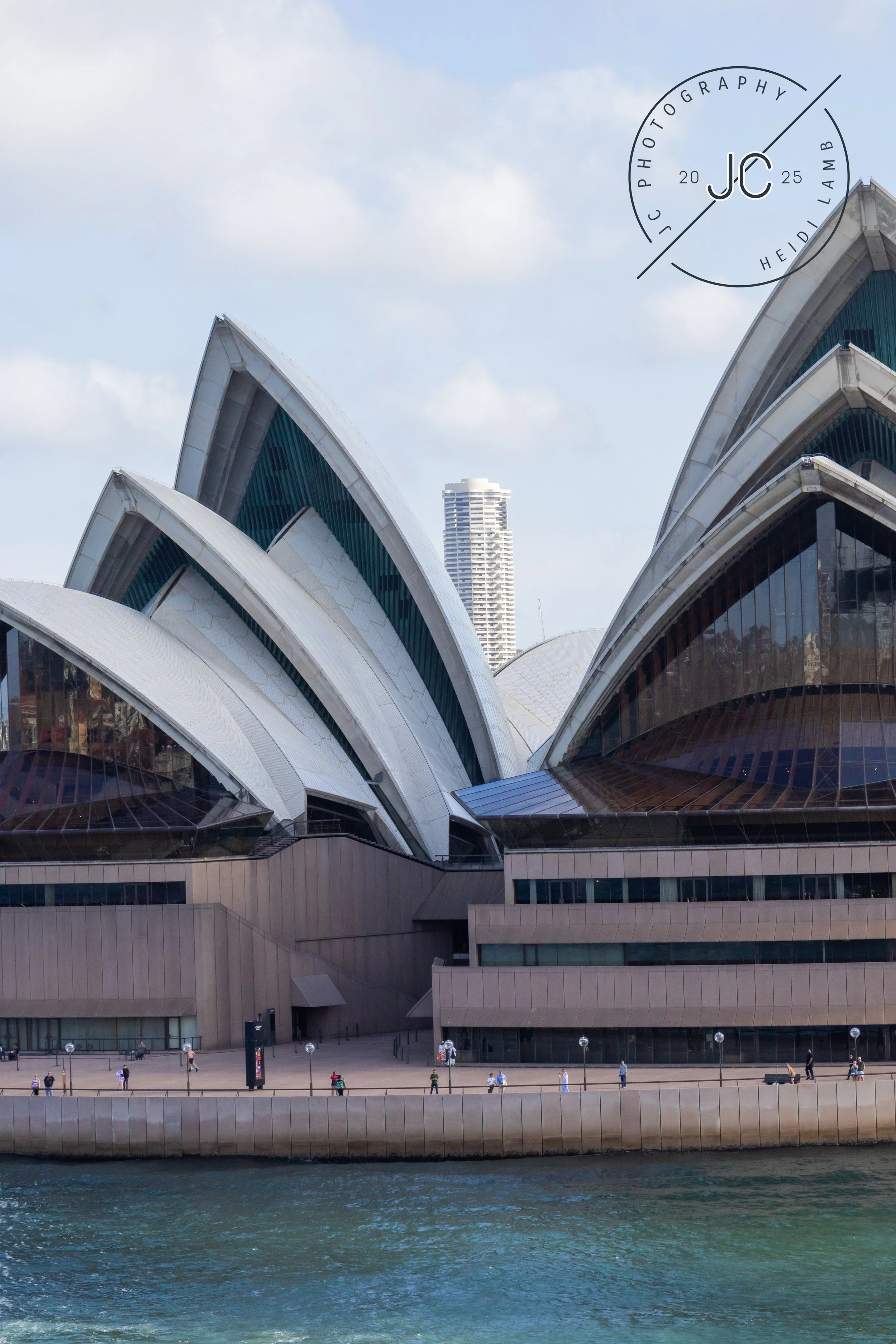 Sydney Opera House with people walking along the waterfront under a partly cloudy sky.