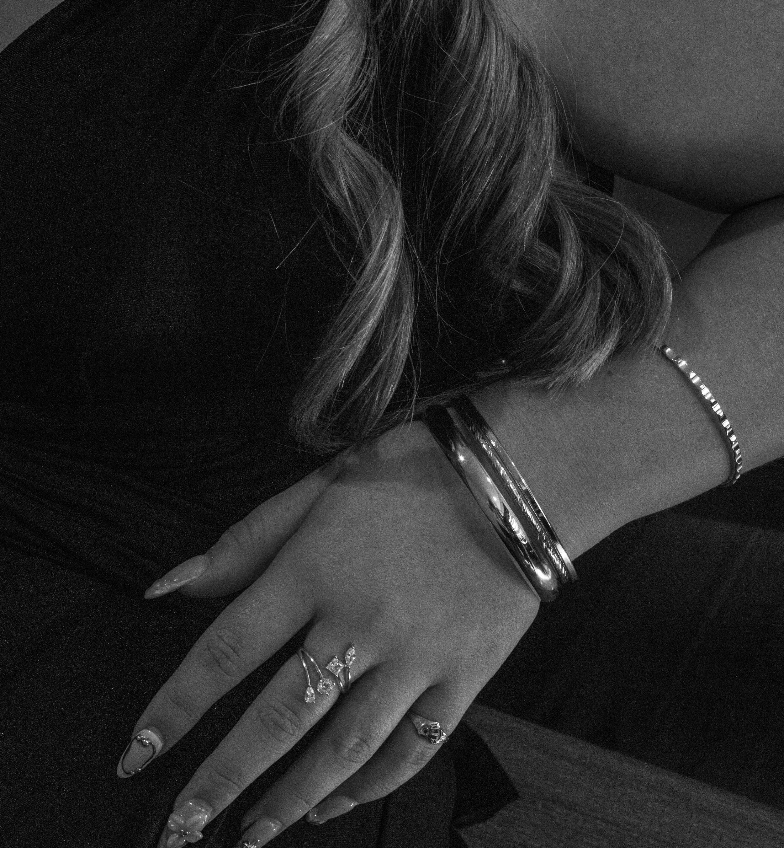 Close-up of a woman's hand resting on her lap, adorned with multiple rings and bangles, with her wavy hair partially visible.