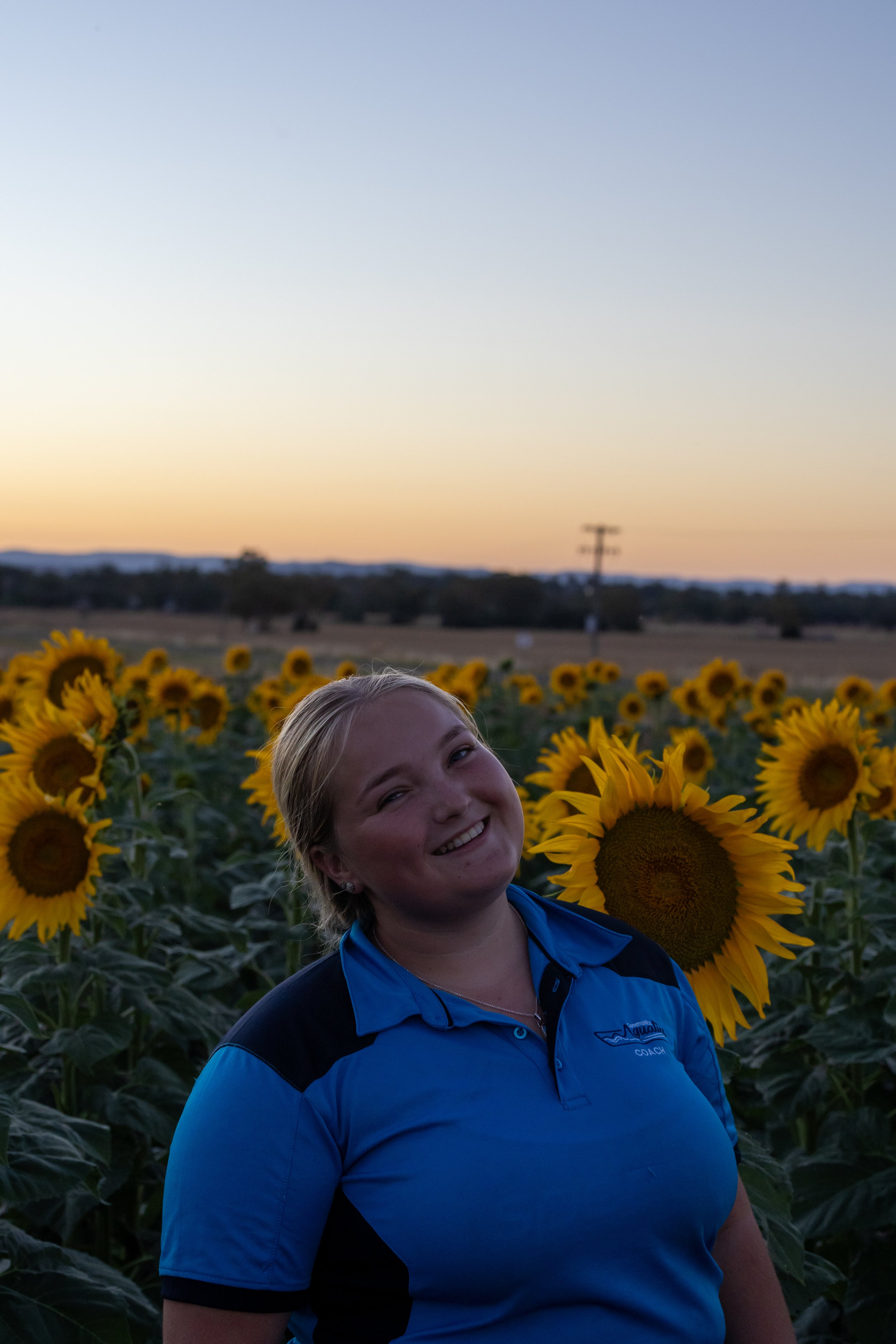 A smiling woman standing in a sunflower field at sunset.