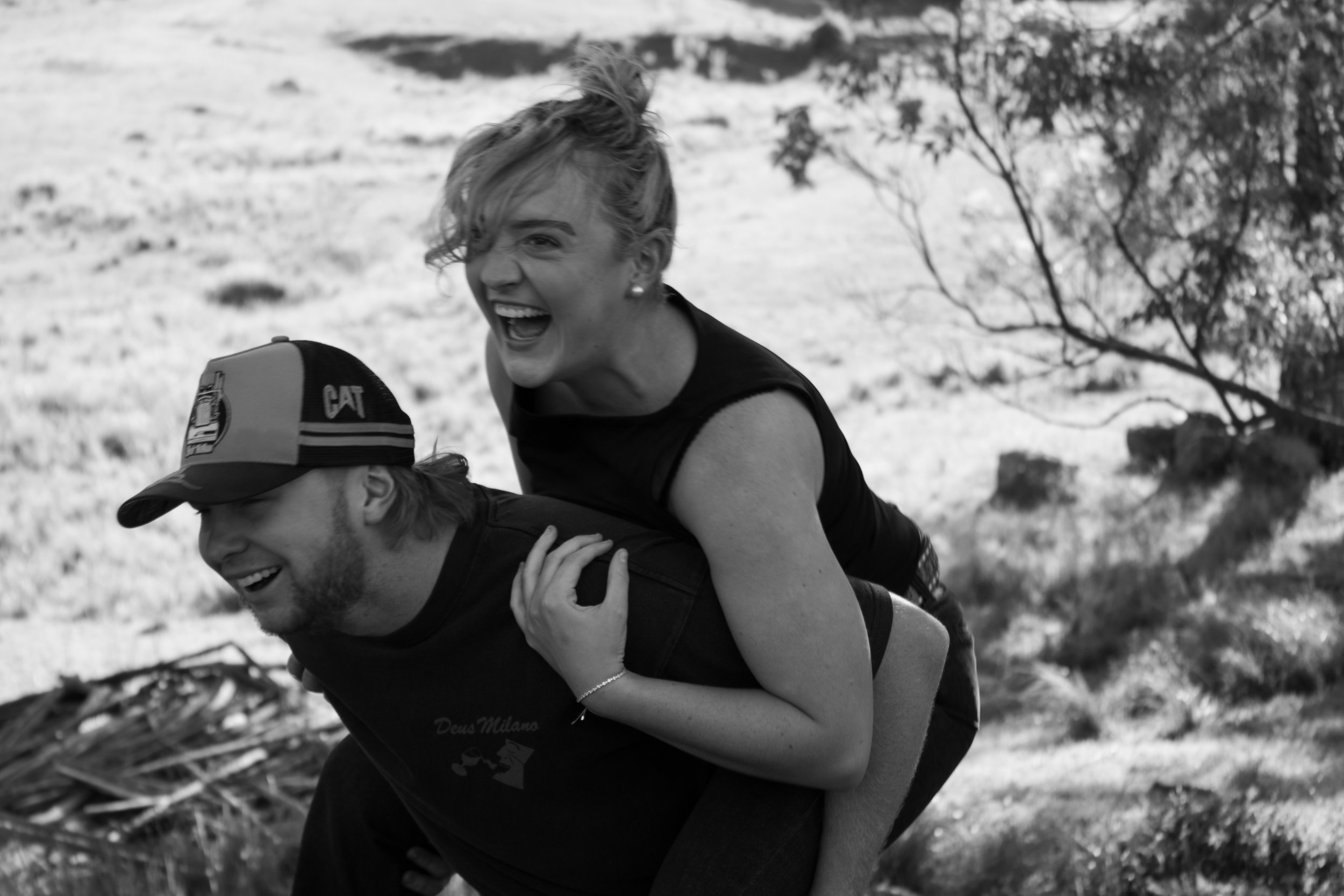 A woman laughing and enjoying a piggyback ride on a man outdoors in a natural setting.