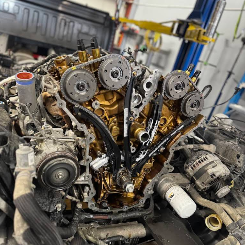 Close-up of a car engine with timing belts and gears exposed, in a workshop setting.
