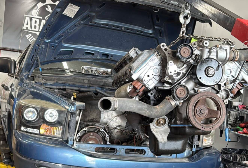 Car with open hood and engine removed, mounted on a stand for repair or replacement at an auto repair shop.